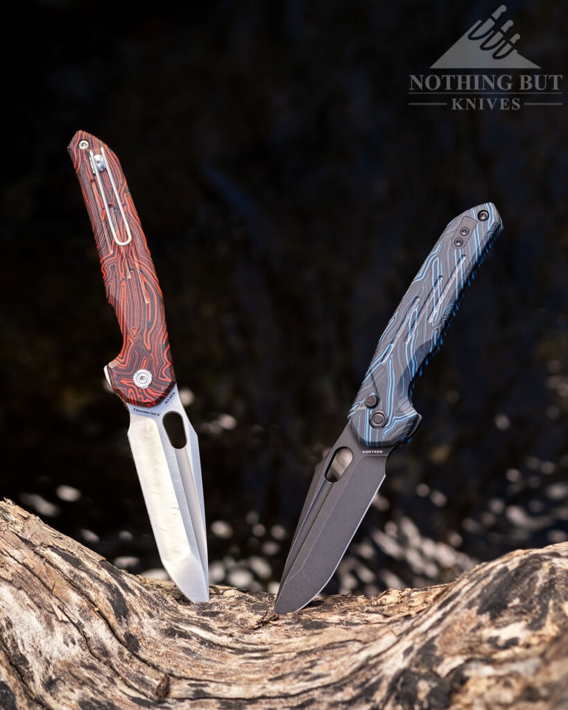 Two versions of the Vosteed Thunderbird pocketknife sticking out of a large piece of driftwood above a creek.