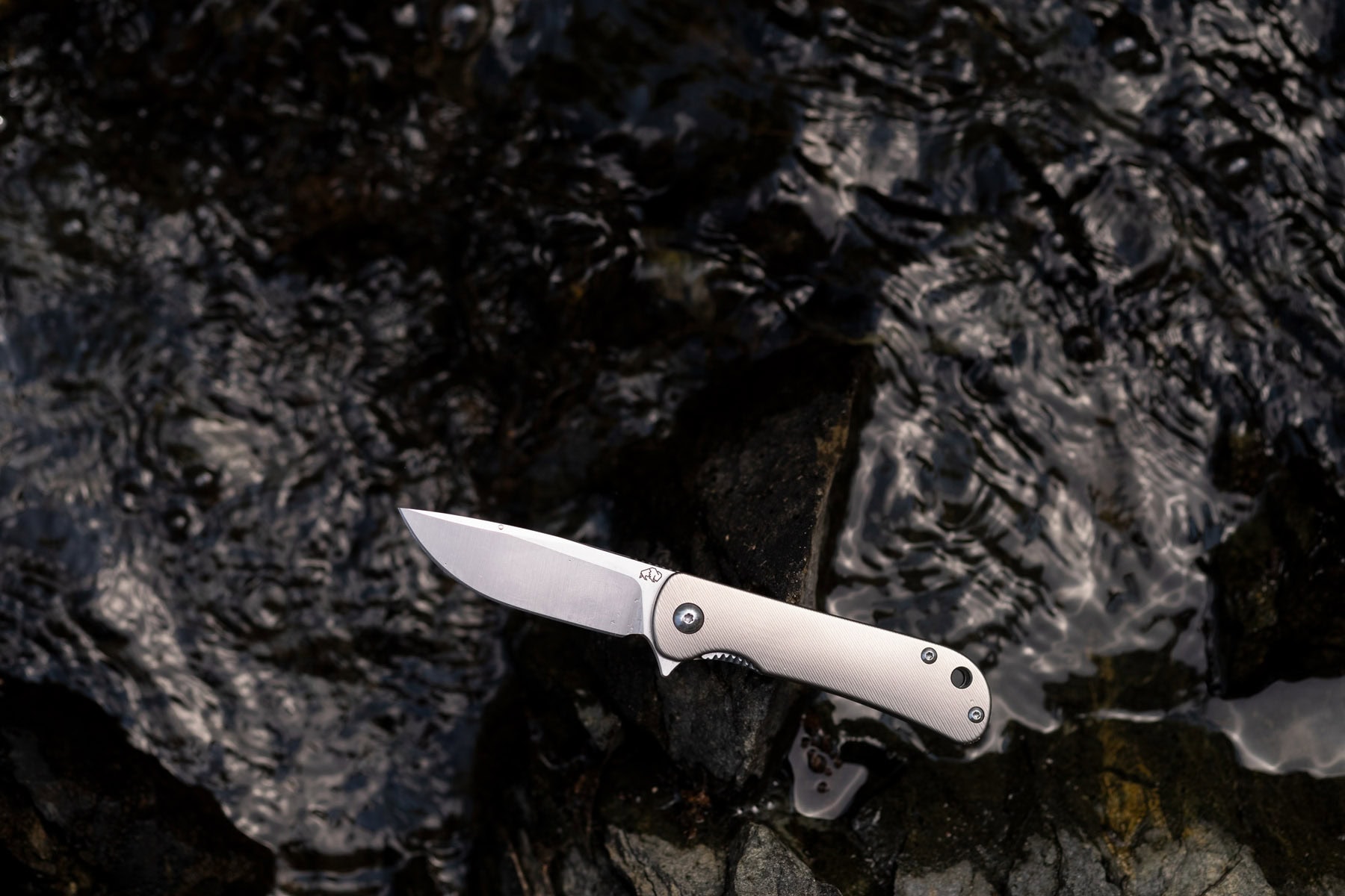 The titanium version Fast Eddie with VG10 steel resting on a rock in a creek. 