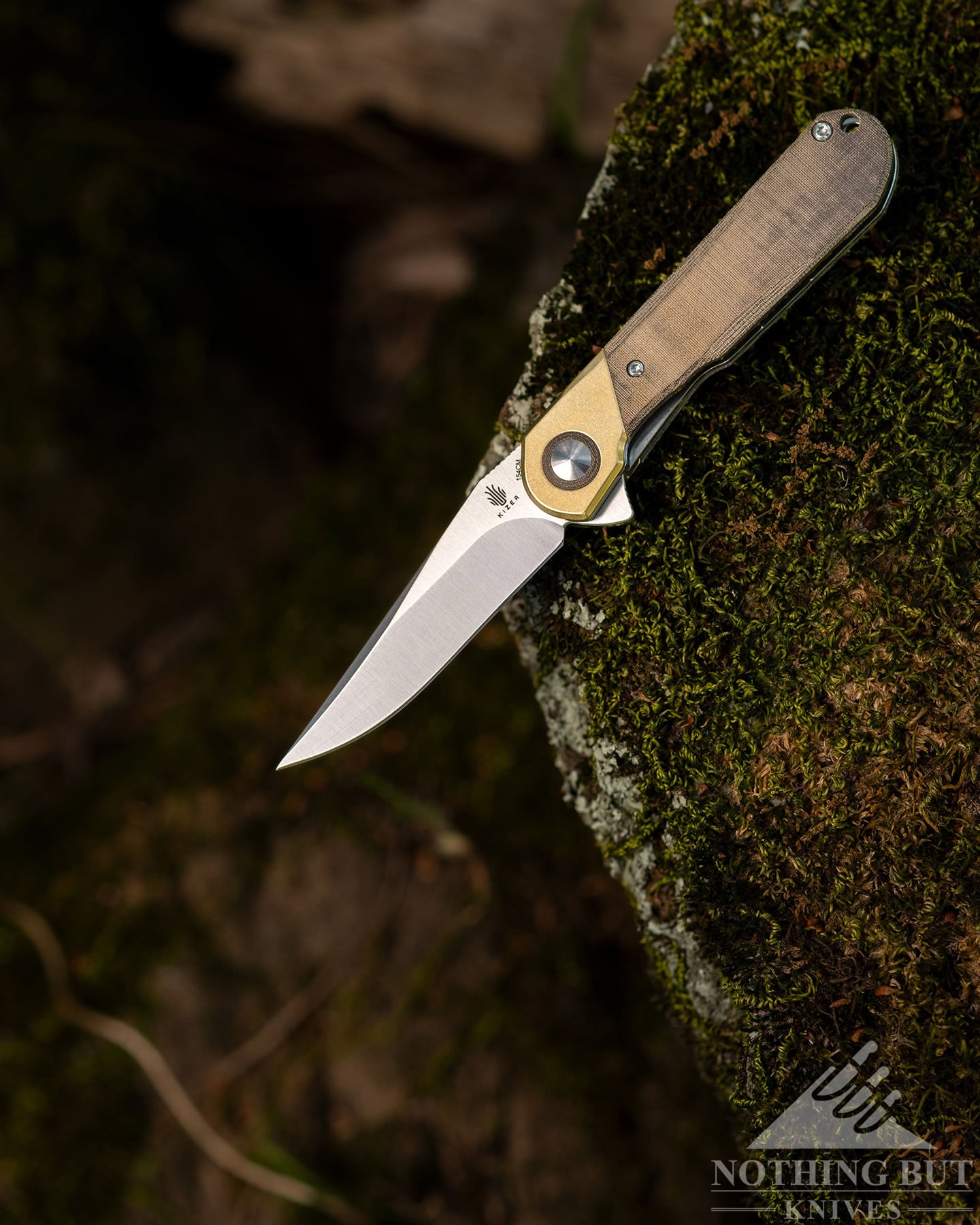 The Kizer Comet sits open on the edge of a mossy rock.