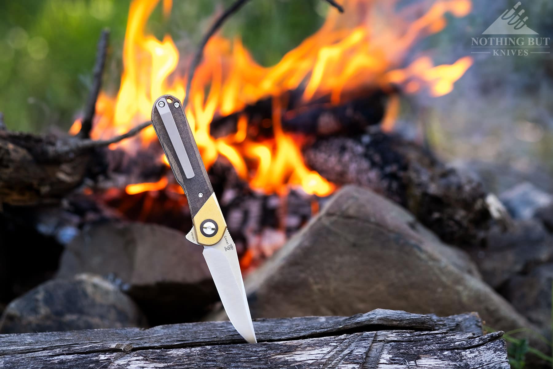 The Kizer Comet stabbed into a charred log in front of a fire.