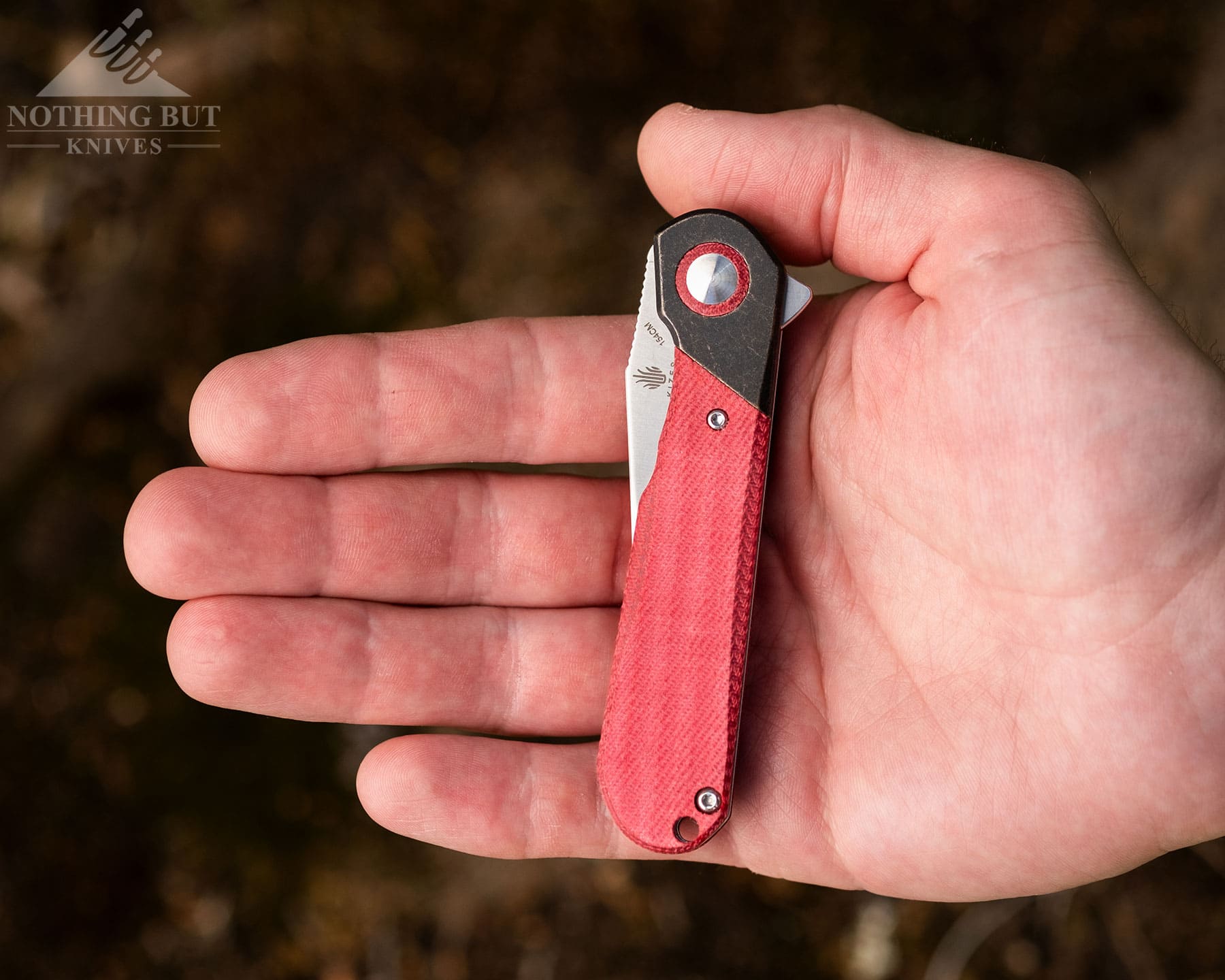The Kizer Comet with red scales sits closed in a hand.