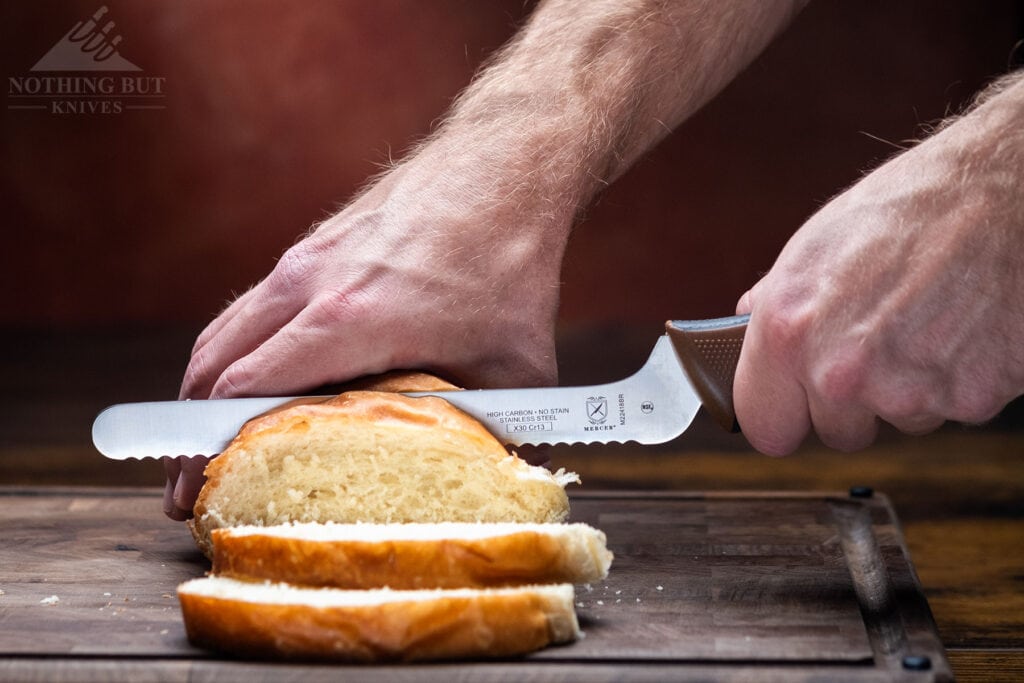 The bread knife cutting slices off of a soft loaf.