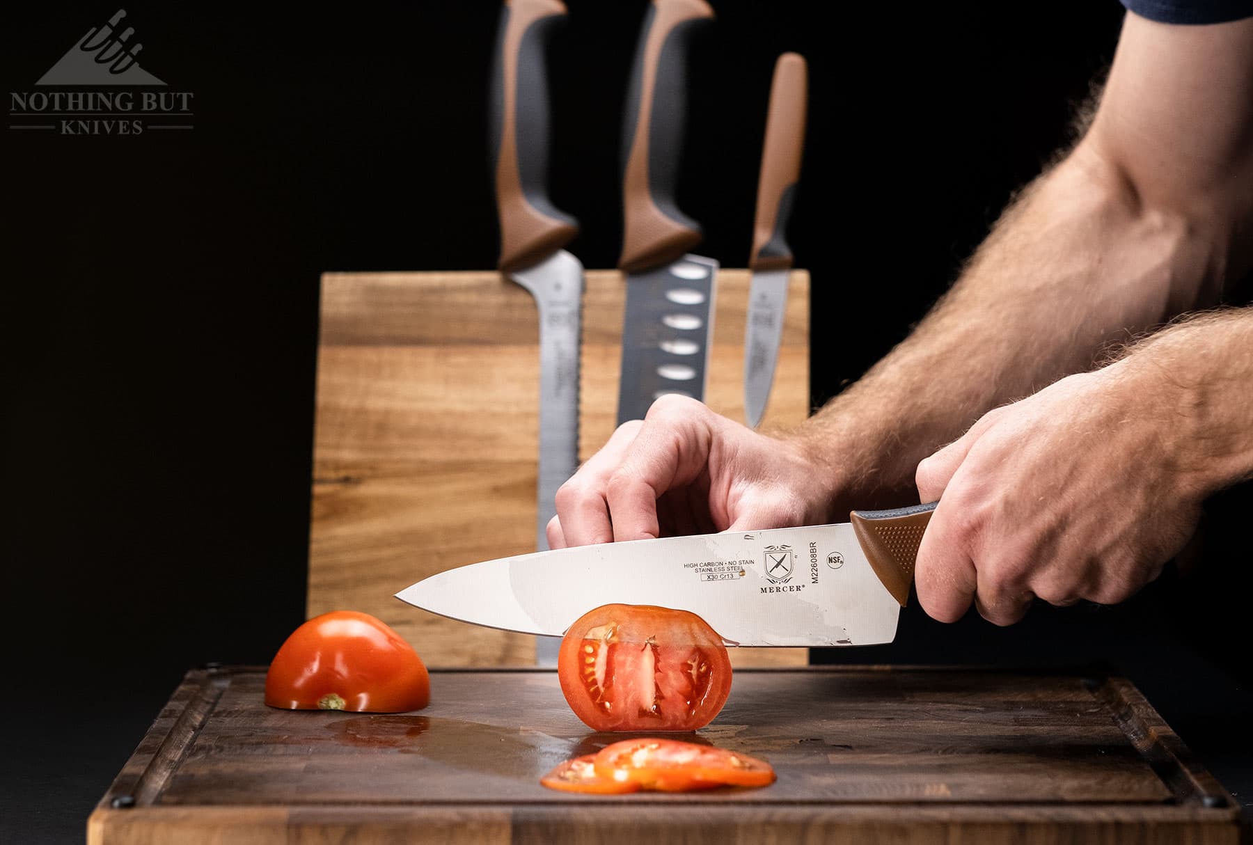 The Mercer Millennia chef's knife cutting a thin slice off a tomato.