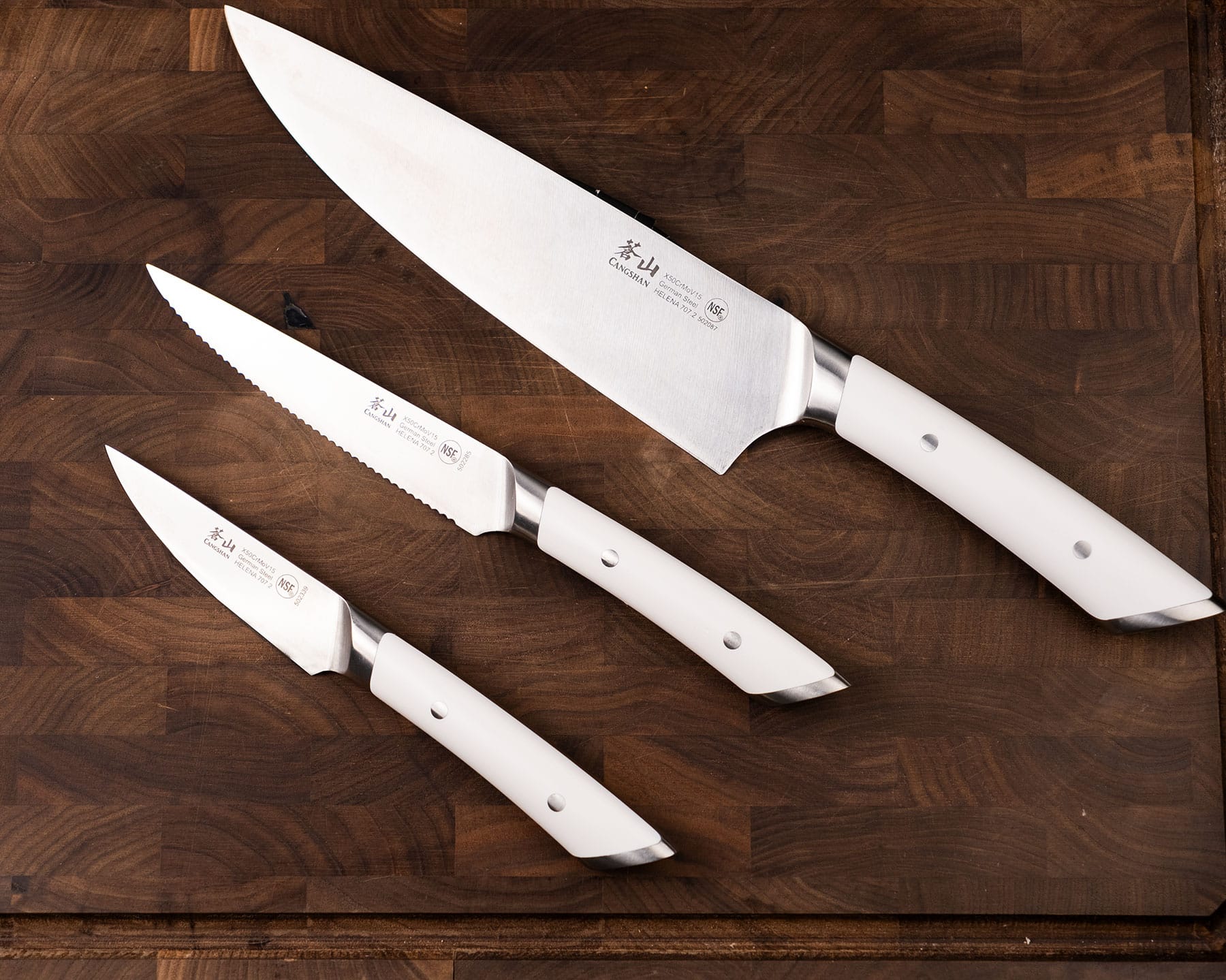 The Cangshan Helena 3 Piece knife set on a dark wood cutting board.