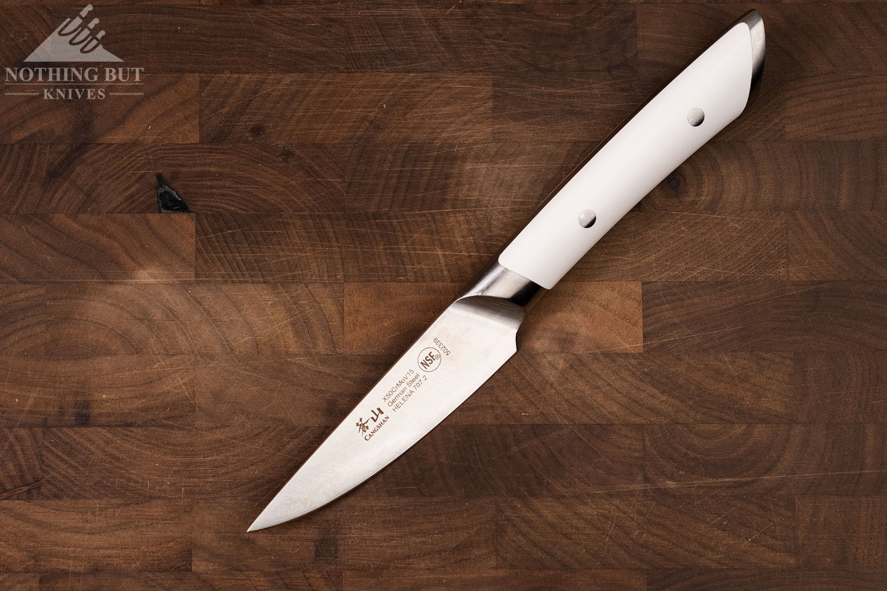 The Cangshan Helena white paring knife on a dark wood cutting board.