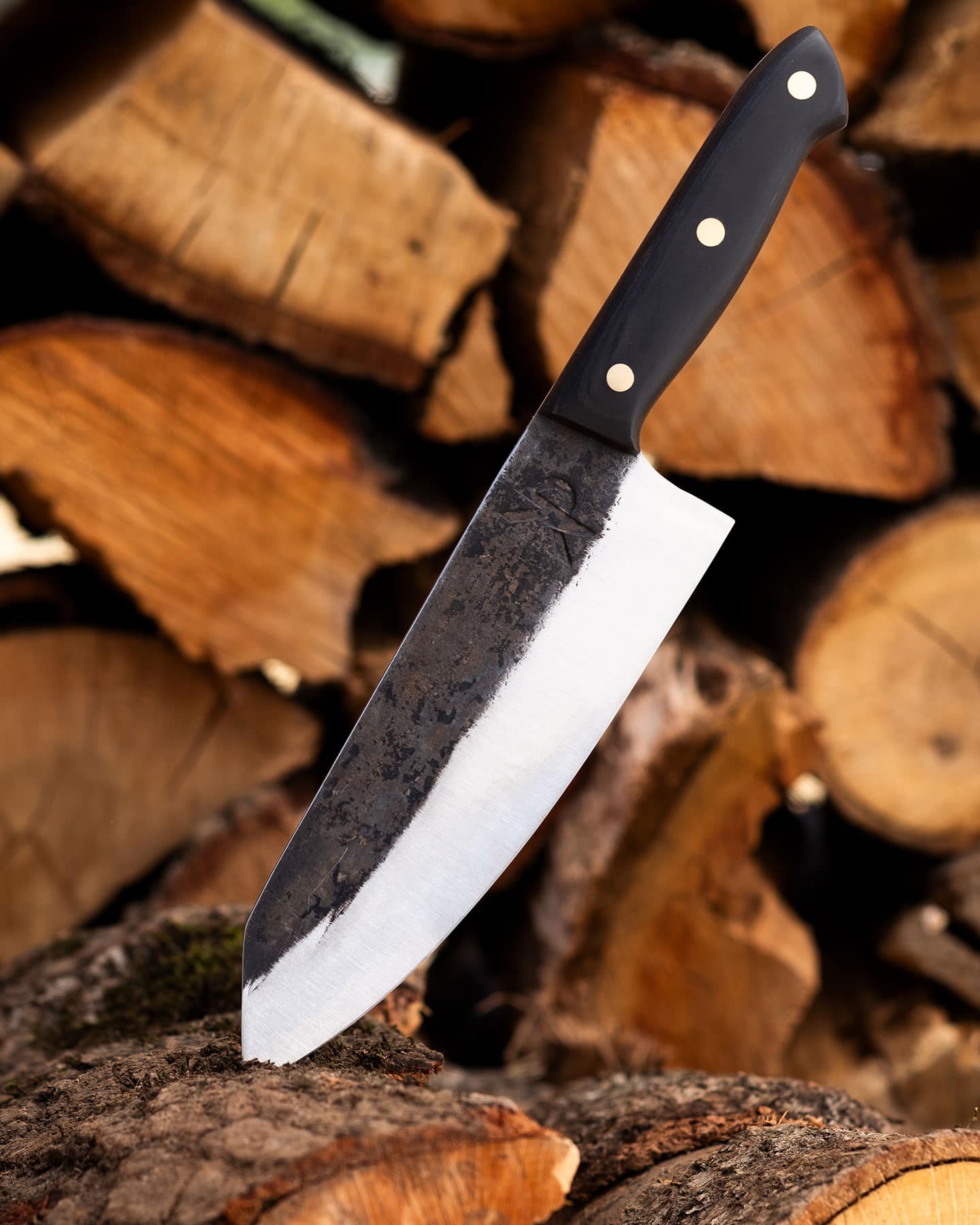 The Kitchen Perfection chef knife sticking out of a log in front of a woodpile.