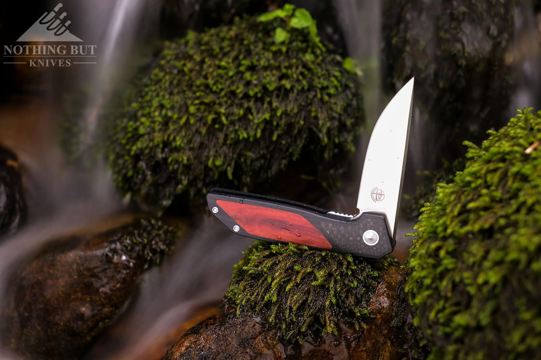 The Begg Knives Diamici on a mossy rock in front of a small waterfall.