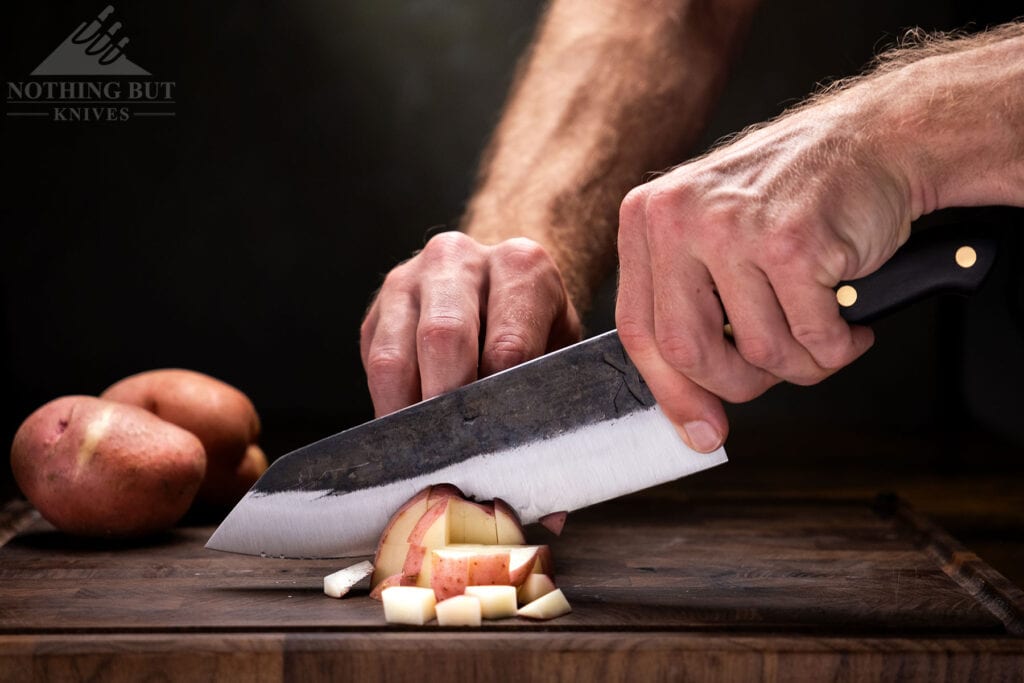 The tough high carbon steel blade of the Kitchen Perfection chef knife slicing potatoes.