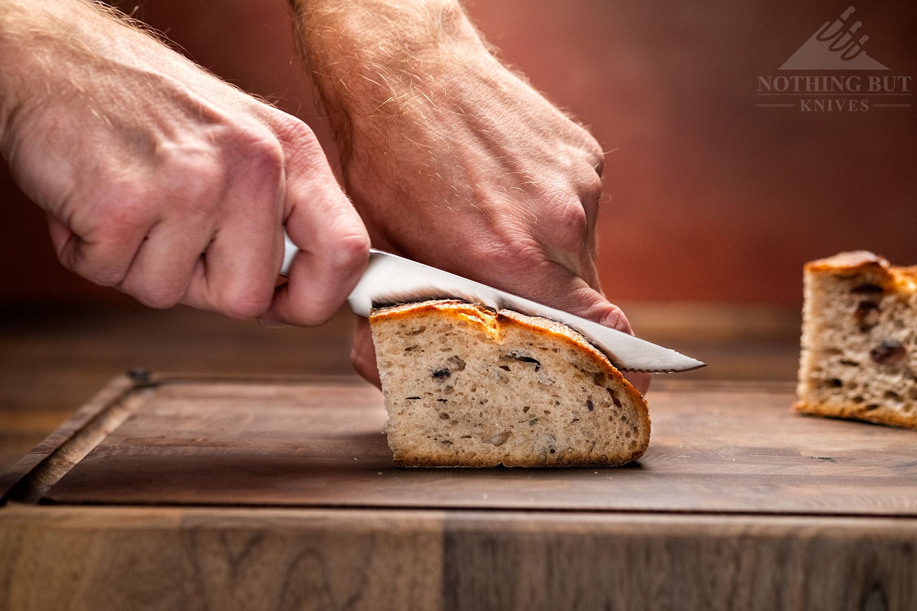 The Cangshan Helena serrated utility being use to slice a loaf of bread. 