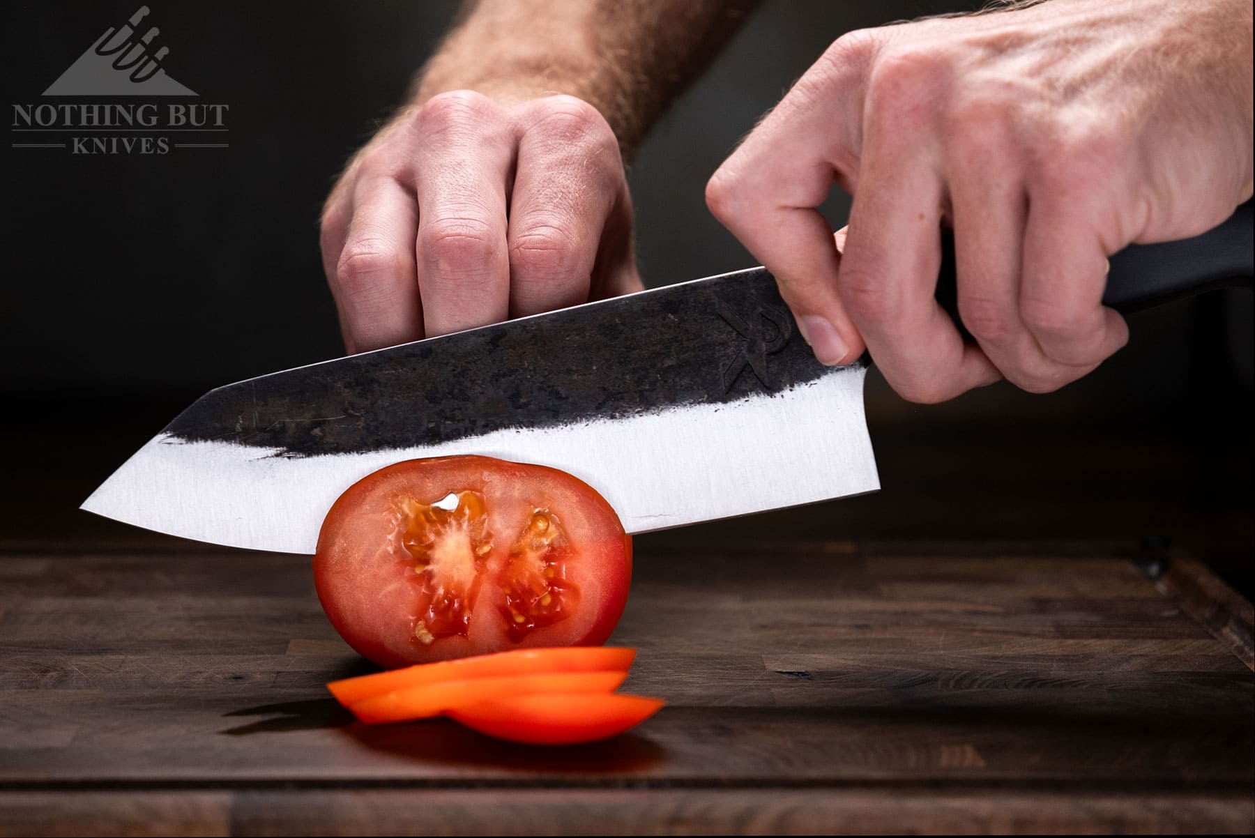 A close-up of a rustic chef knife slicing a tomato. 