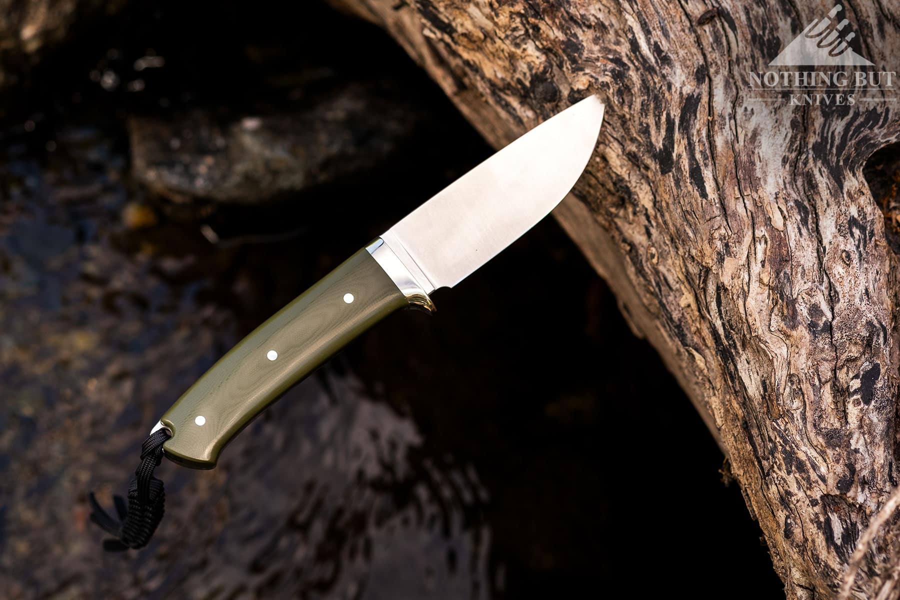 A profile view of the Civivi Cloud Peak knife sticking out of a log above a creek.