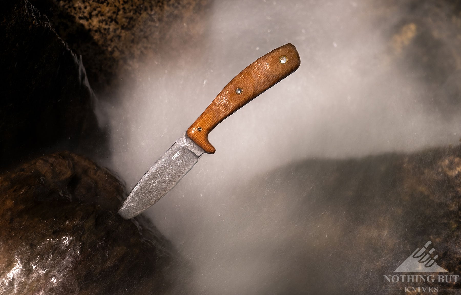 The CRKT Soldotna sticking out of a piece of driftwood in a mountain creek. 