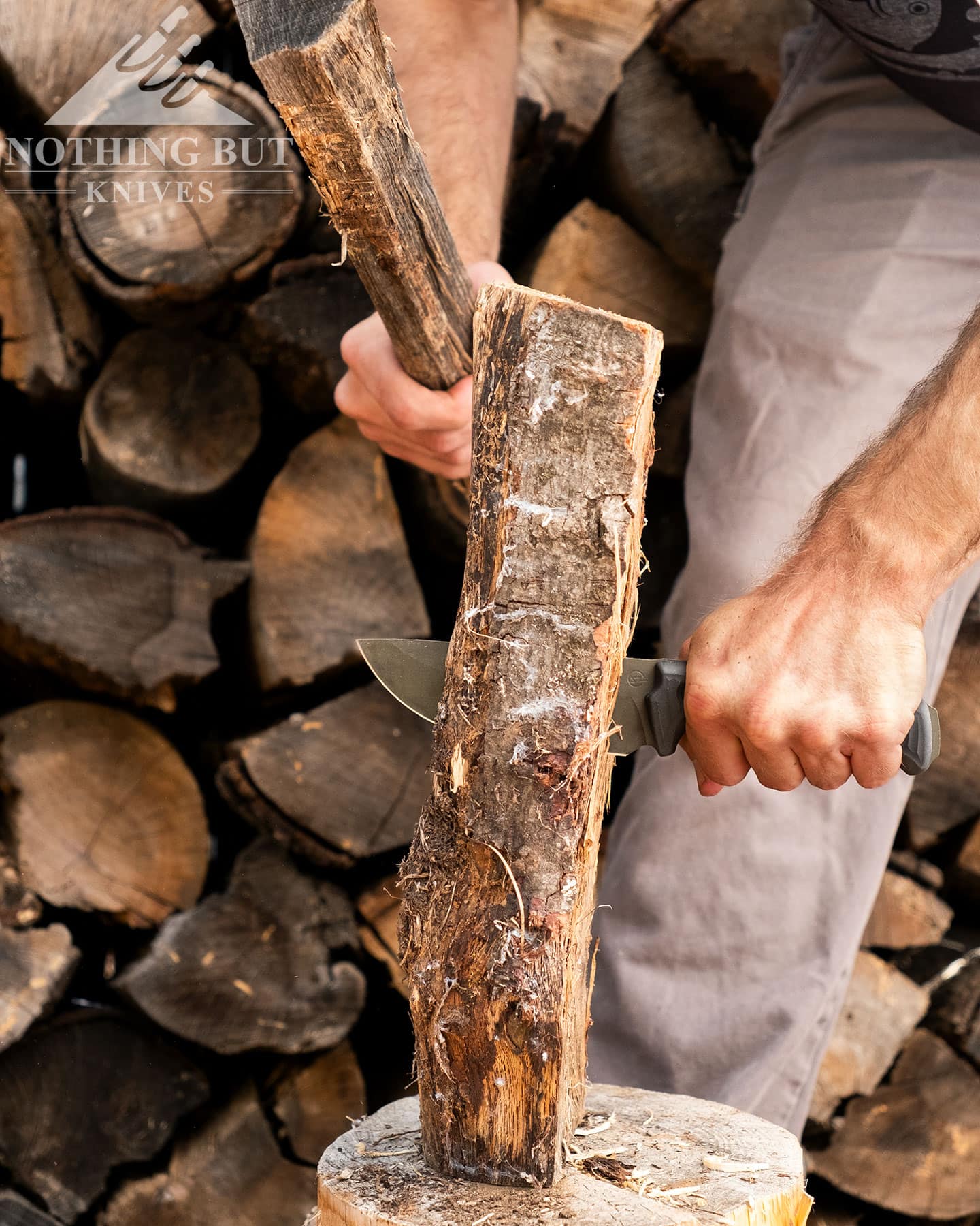 The Schwarz Knives Lost Trail 5 camp knife being used to baton a piece of Oak firewood in front of a woodpile.