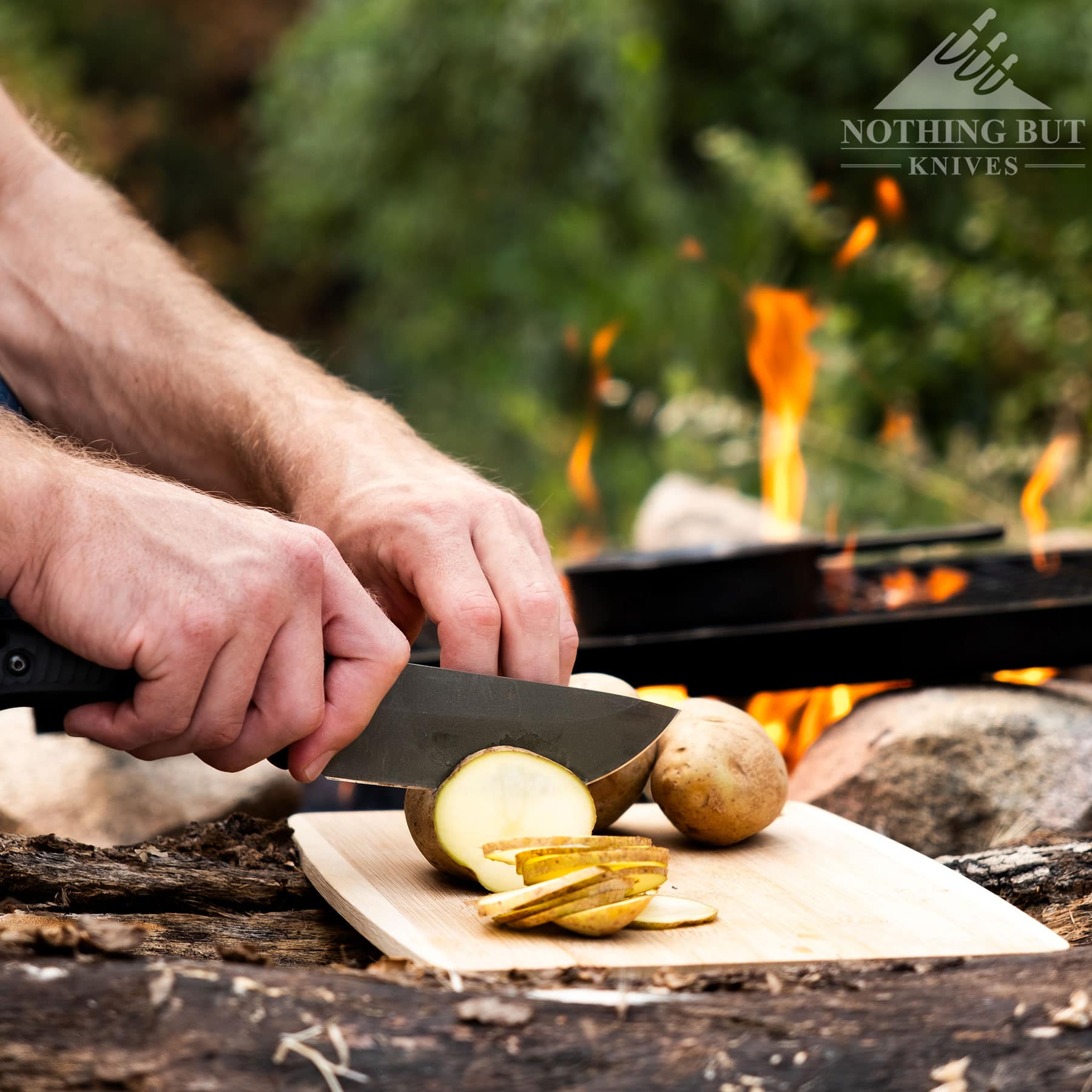 The Schwarz Lost Trail 5 knife being used to slice a potato in front of a campfire.