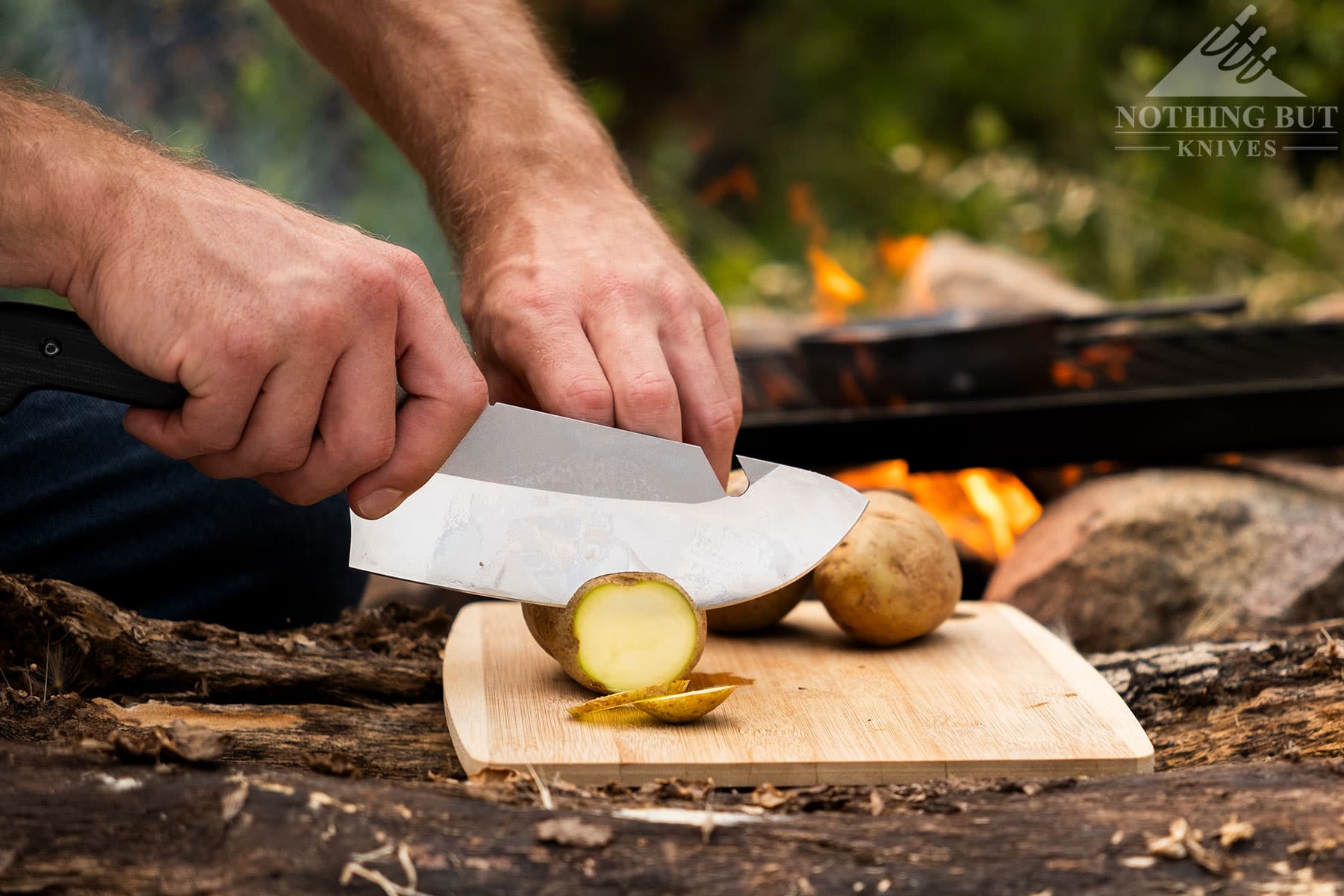 A close-up of the Maxsa Blade camping chef knife slicing a potato in front of a campfire. 