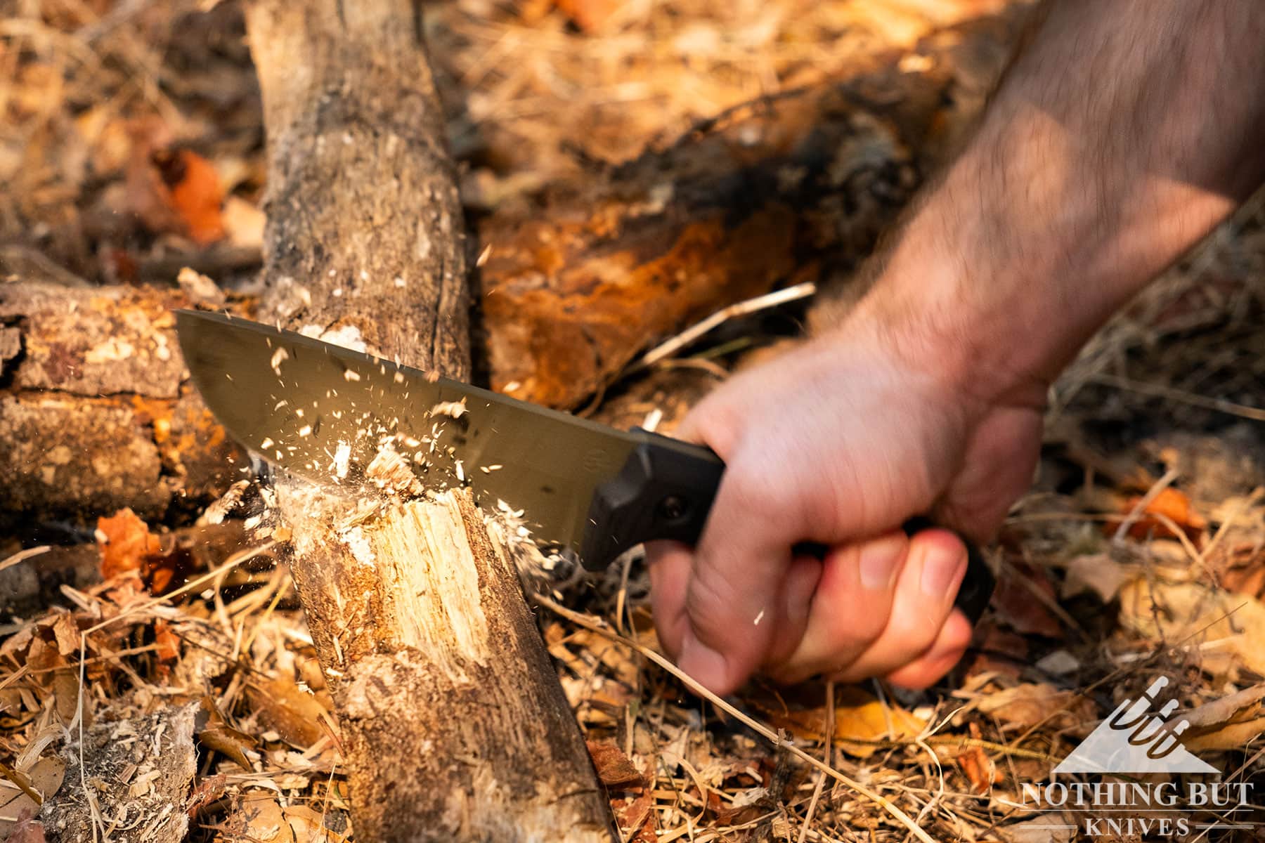 The American made Lost Trail 5 camping knife being used to chop a log in the middle of a grassy field.