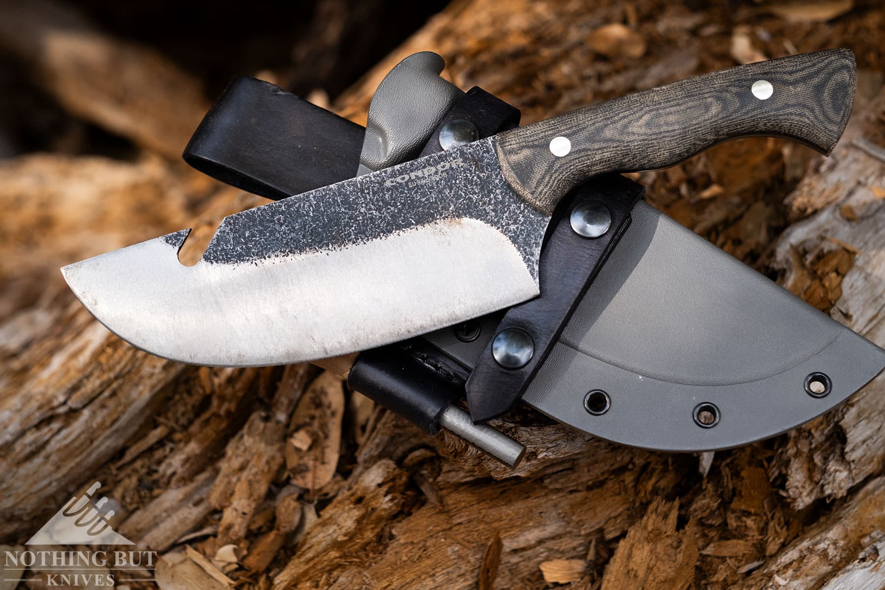 The Condor Bush Slicer fixed blade knife shown here with its sheath on a lof outdoors.