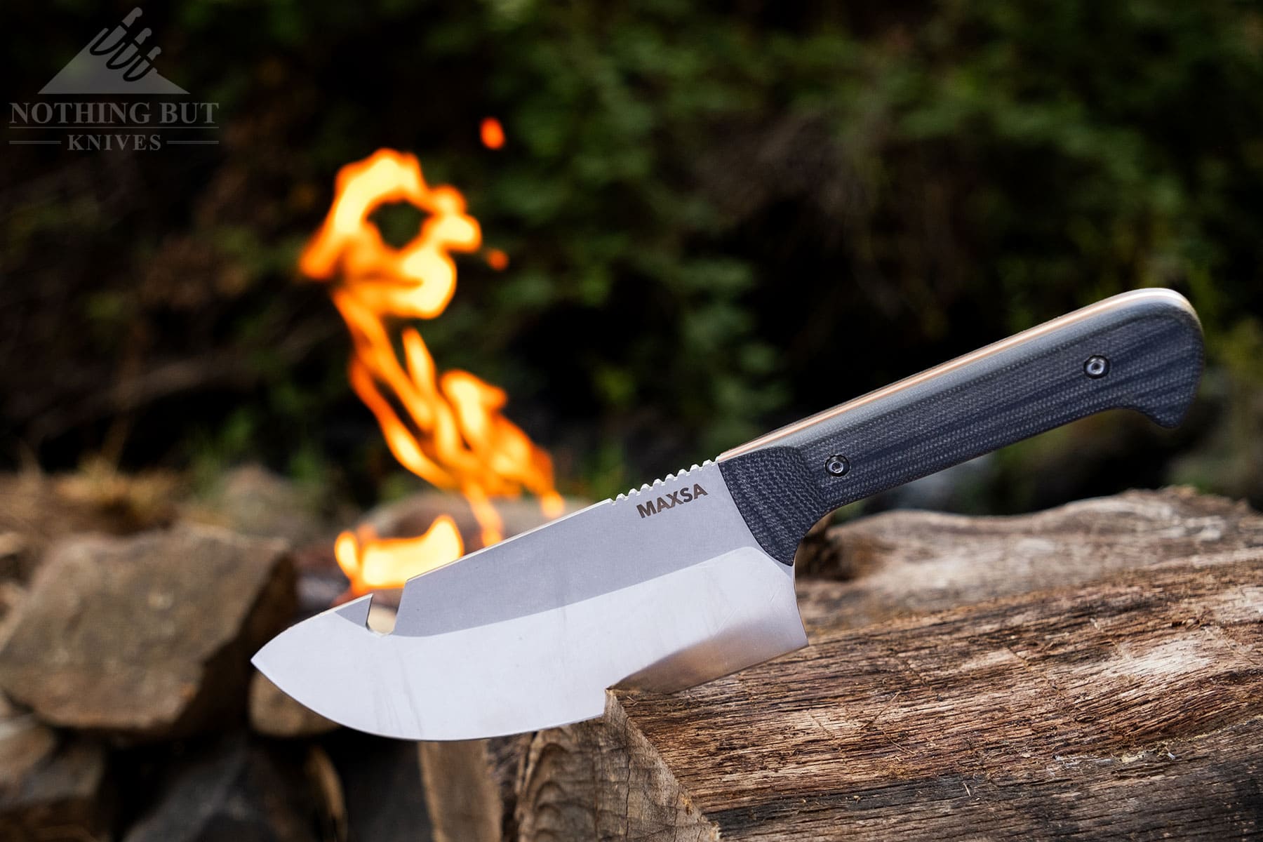 The Maxsa fixed blade knife with the blade wedged into a log in front of a campfire.