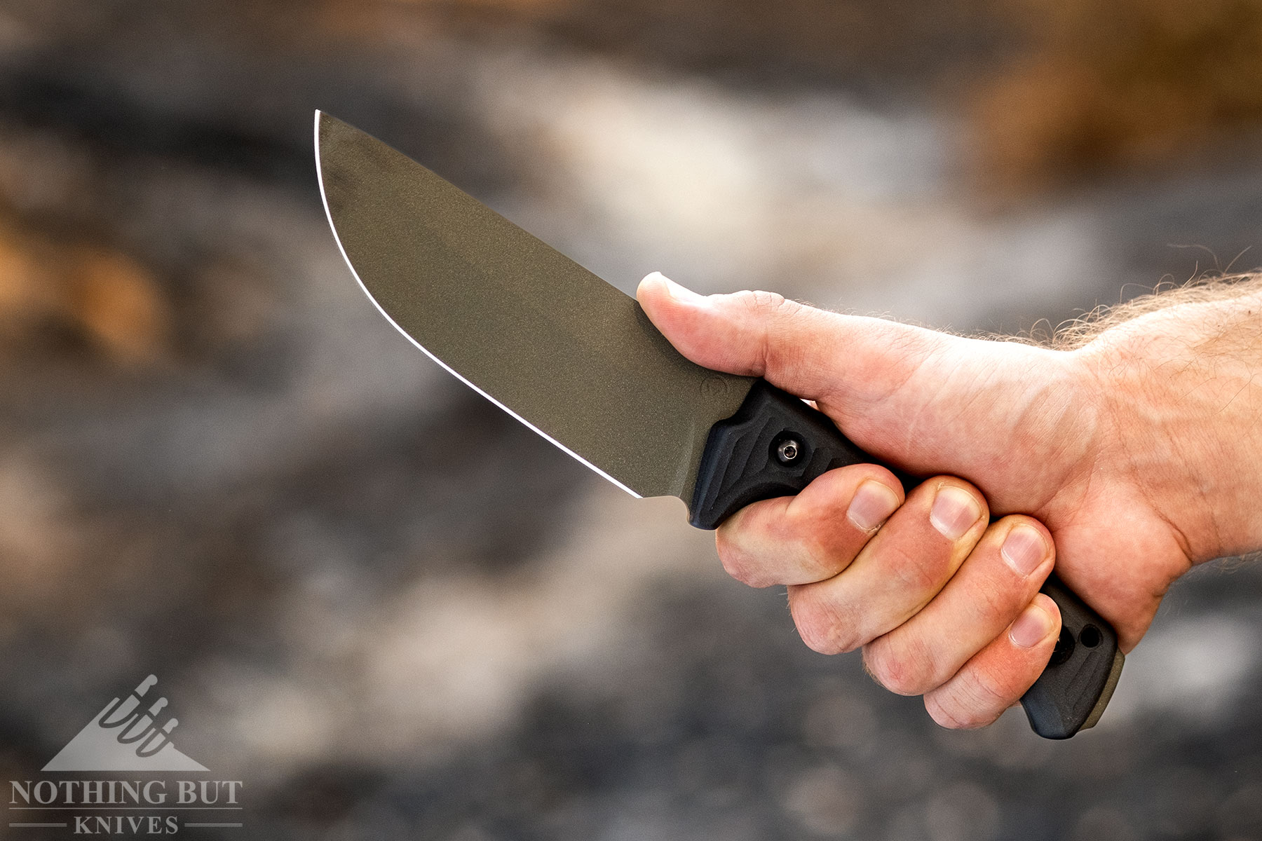 The Schwarz Knives Lost Trail 5 knife being gripped in a person's right-hand outdoors. 