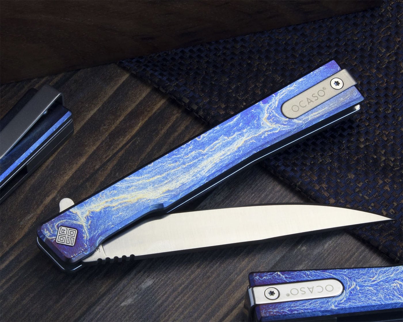 The anodized titanium version of the Ocaso Solstice with the blade partially open on a wood table. 