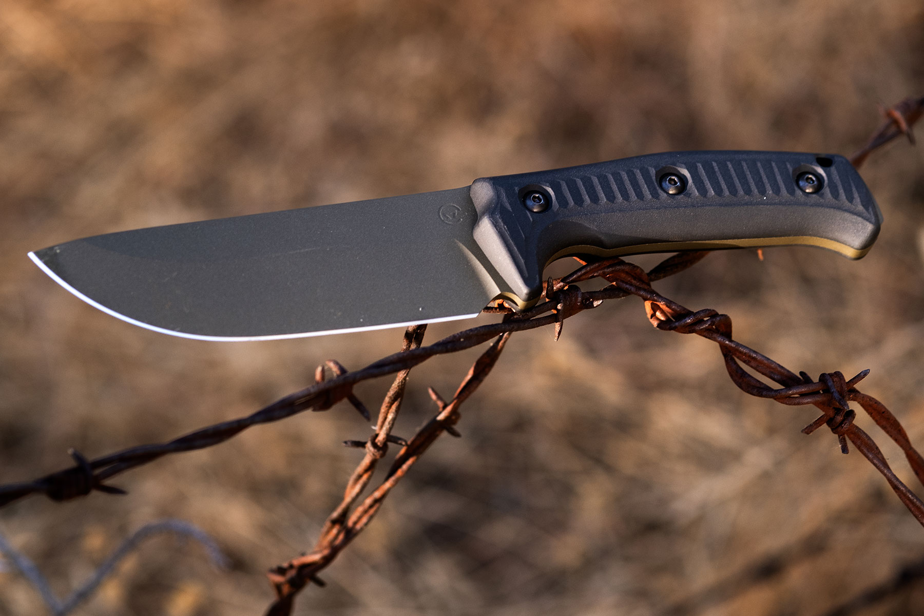 The Schwarz Lost Trail 5 fixed blade knife balanced on a rusty barbed wire fence.