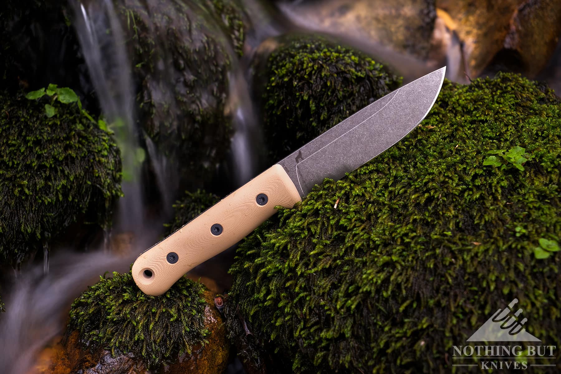 The Reiff F5 field knife on a mossy rock in front of a small waterfall in a mountain creek. 