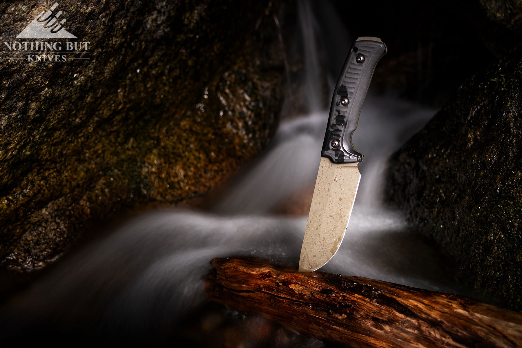 The Schwarz Knives Lost Trail 5 fixed blade sticking out of a piece of driftwood next to a mountain creek to test its corrosion resistance.