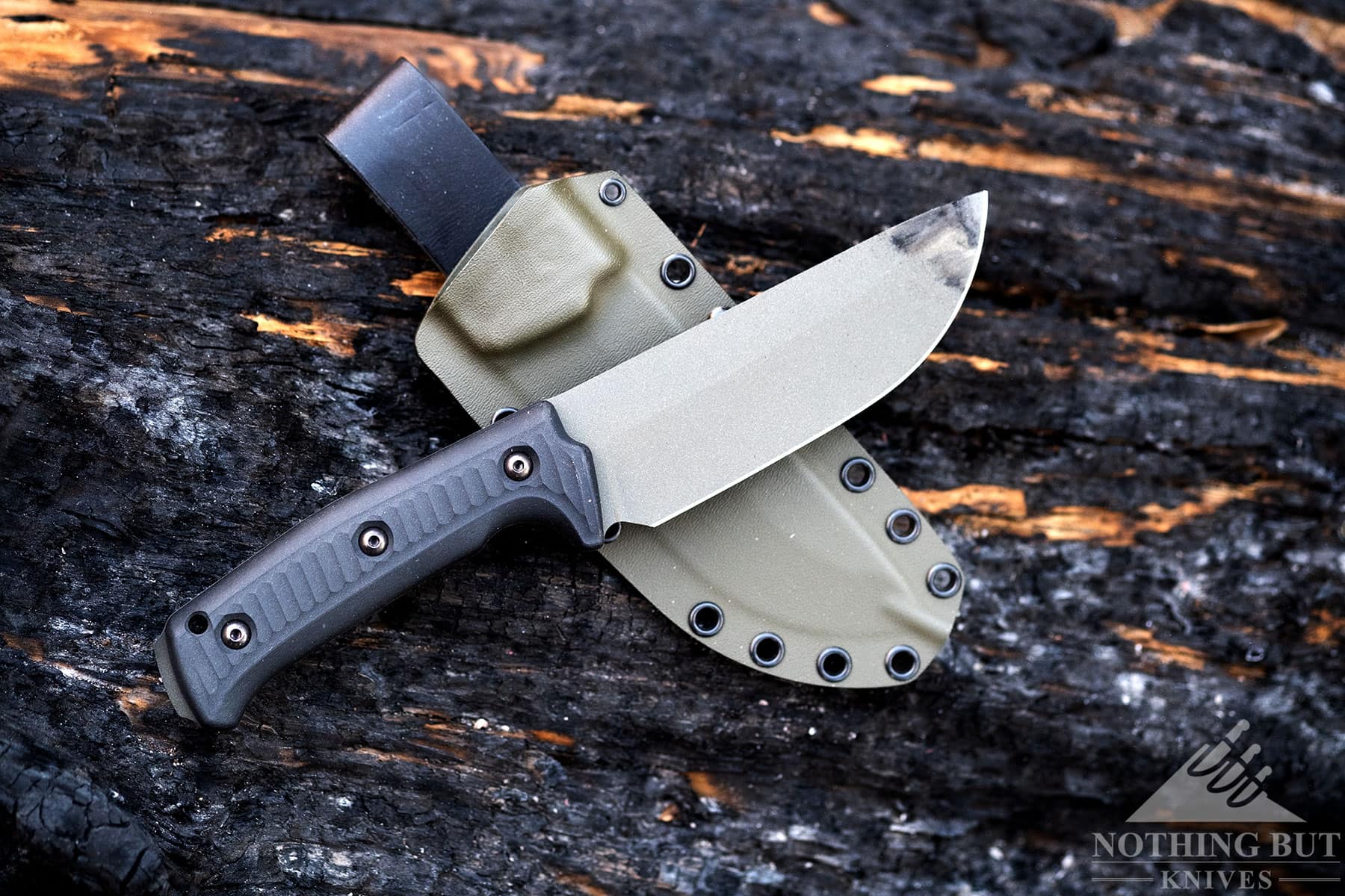 The Lost Trail 5 camp knife shown here with its OD green kydex sheath on top of a charred log.