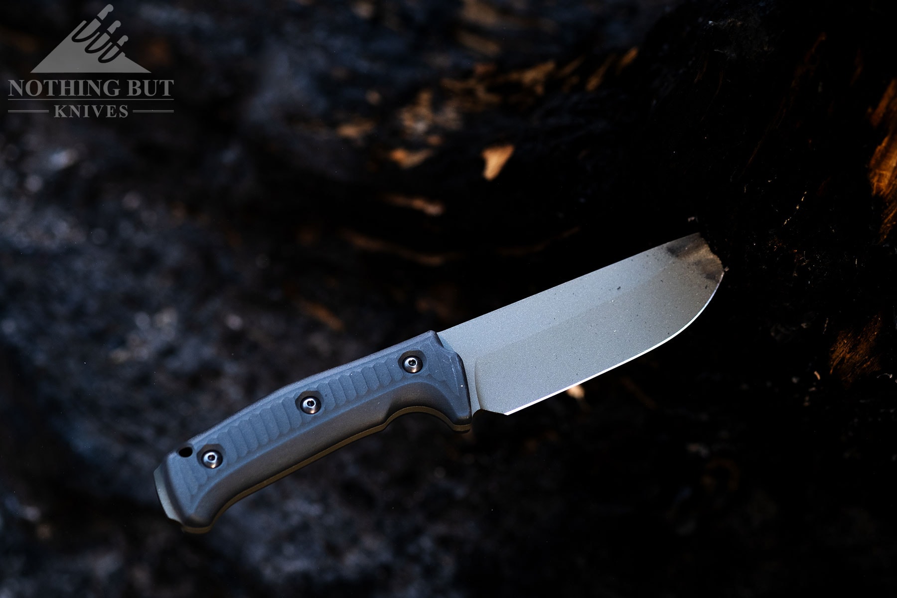 The OD green version of the Lost Trail 5 camp knife sticking out of a charred log. 