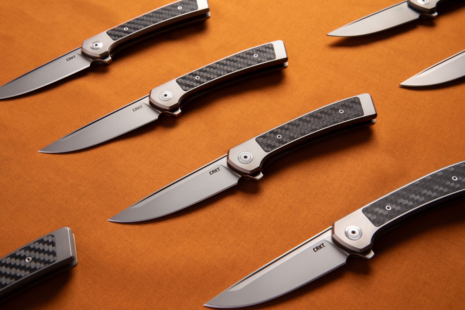 Four CRKT Q frame locks with their blades open on an orange background. 