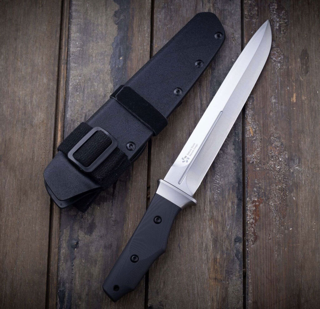 The Katsu FB02 dagger laying next to its empty kydex sheath on a weathered wood surface.