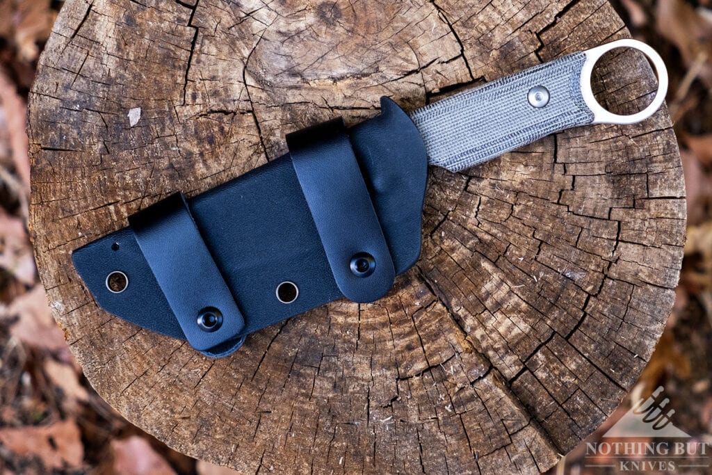 An overhead view of the Kizer Cabox fixed blade inside its kydex sheath on top of a tree stump. 