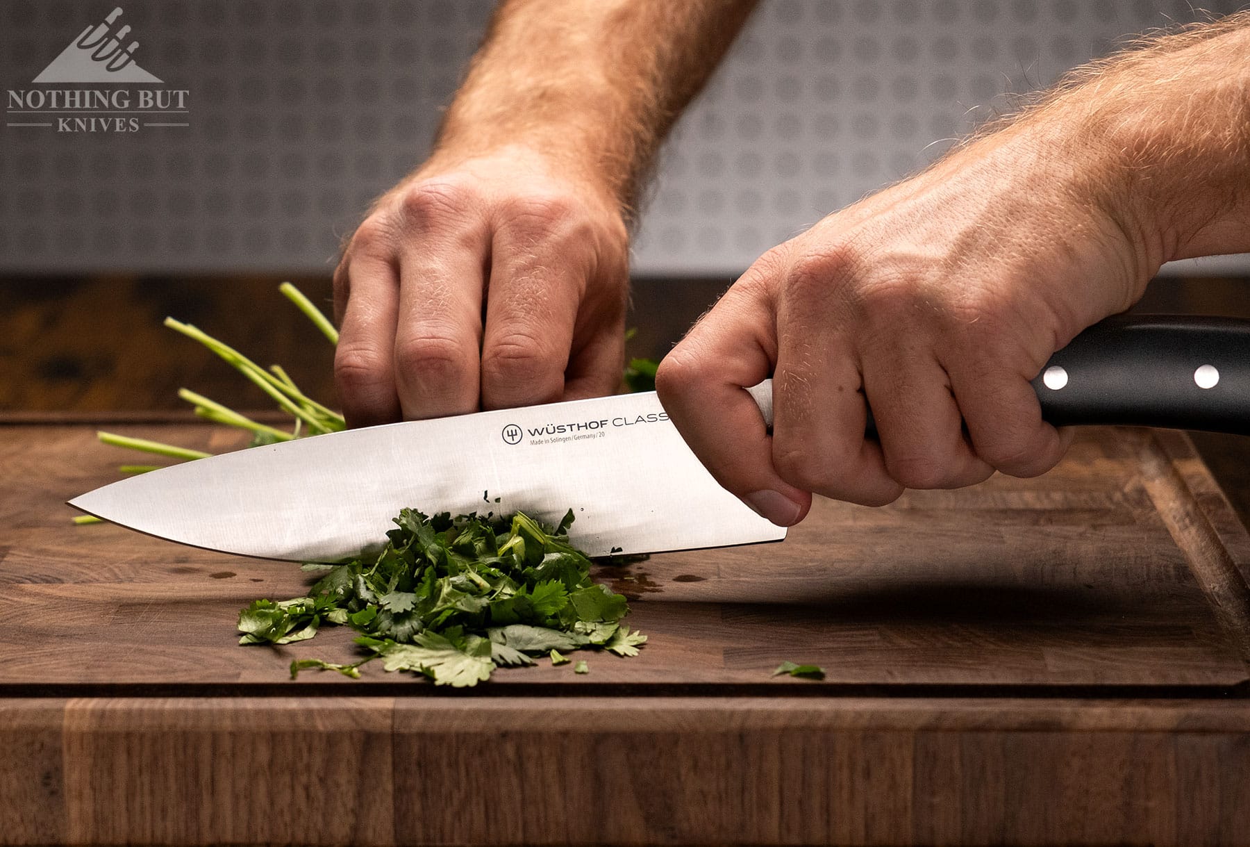 The Wusthof Classic Ikon chef knife being used to dice herbs on an end grain cutting board.