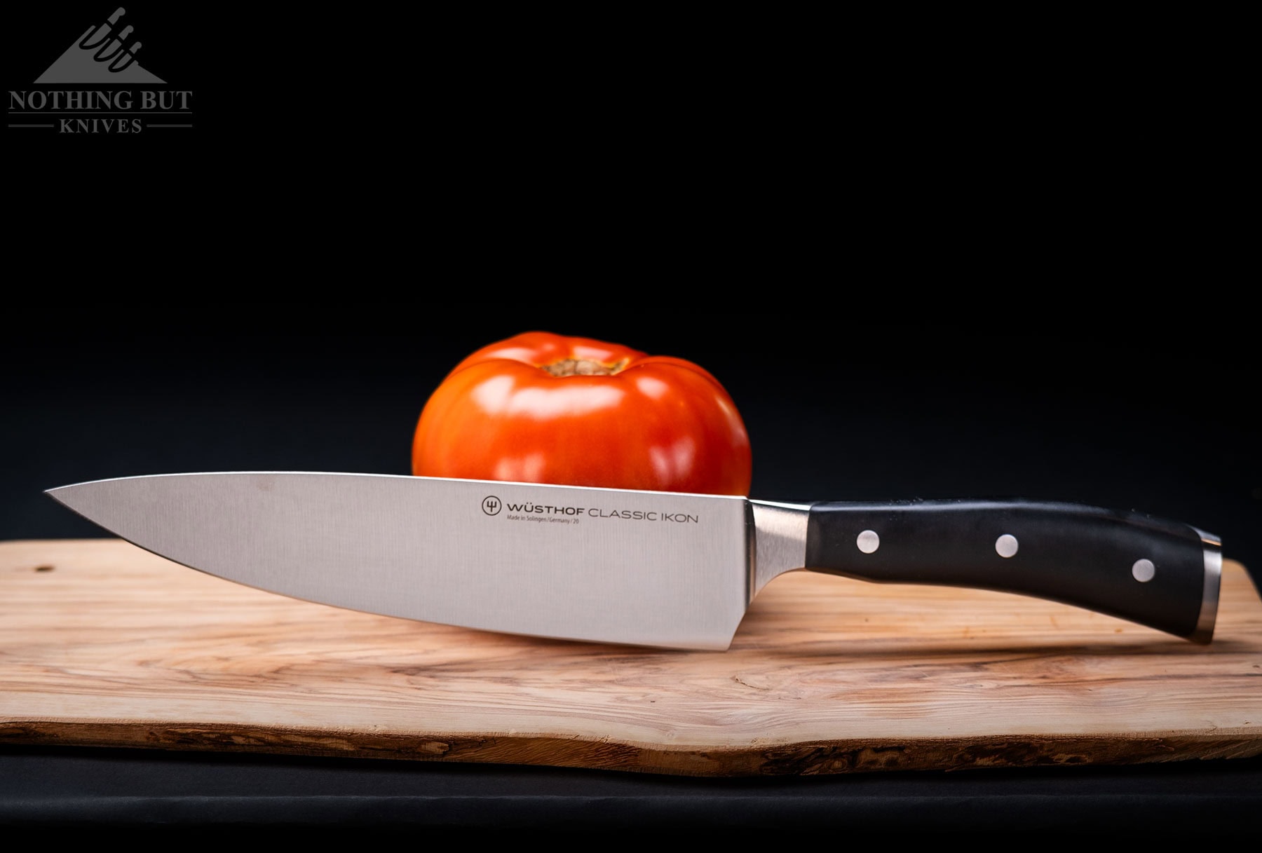 The Wusthof Classic Ikon 8 inch German chef knife leaning against a tomato on an end grain cutting board.