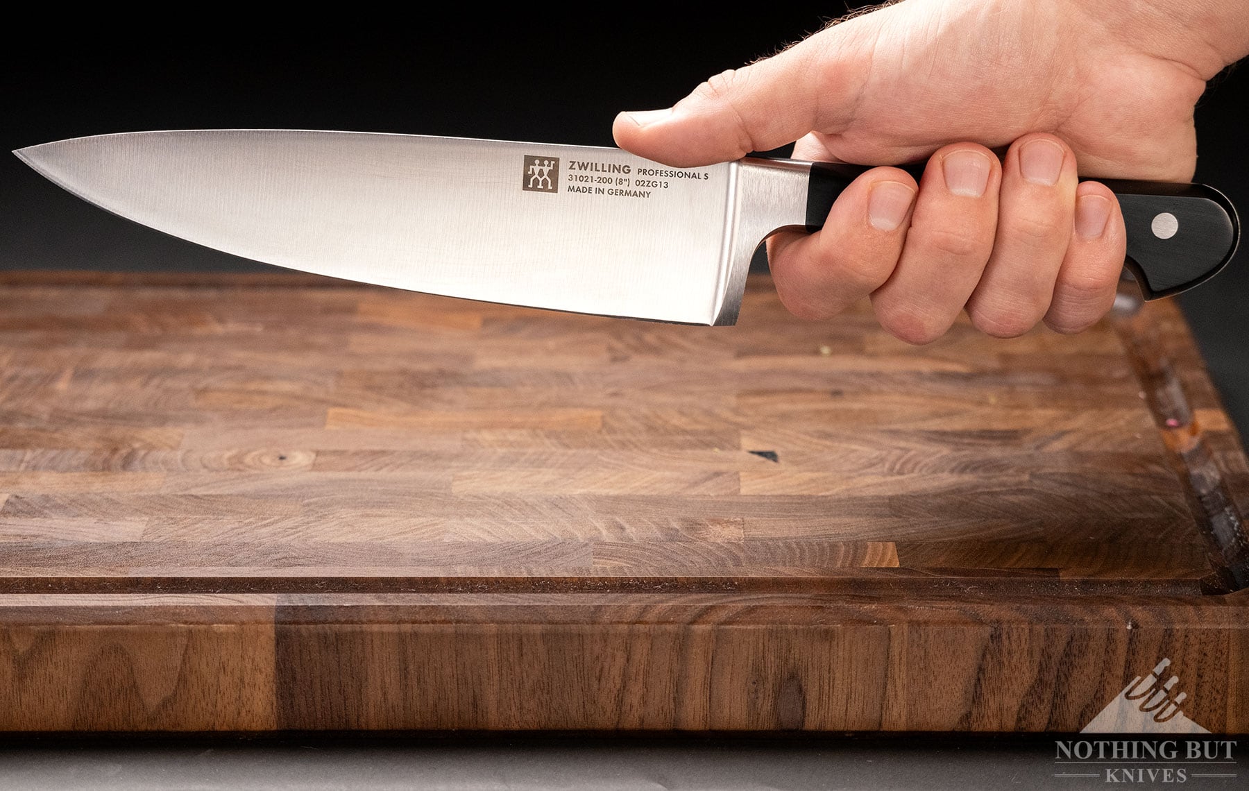 The Zwilling Professional S chef knife being gripped in a person's right hand above an end grain cutting board. 