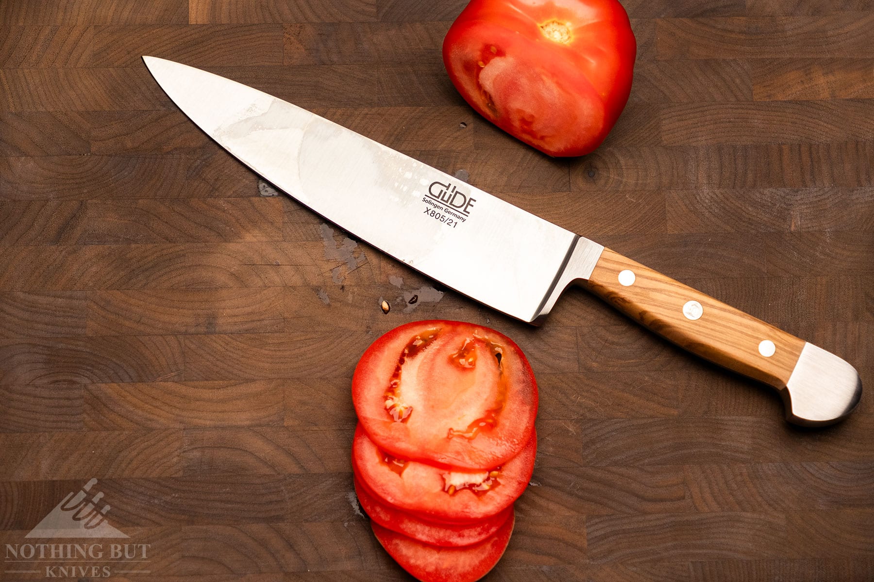 An overhead view of the Gude Alpha chef knife between sections of a tomato it was used to slice.