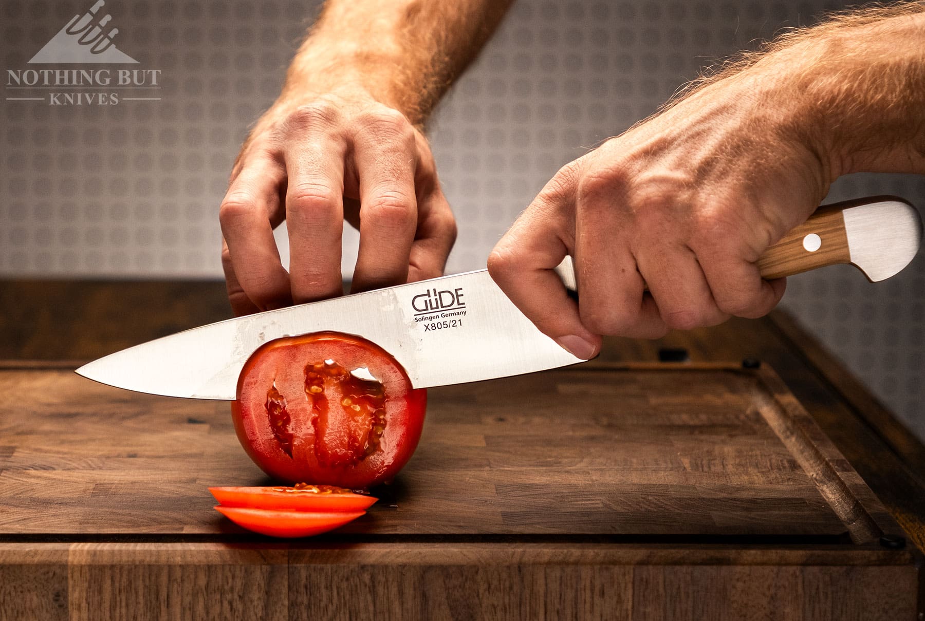 The Gude Alpha 8 inch chef knife being used to slice a tomato in front of an off-white background.