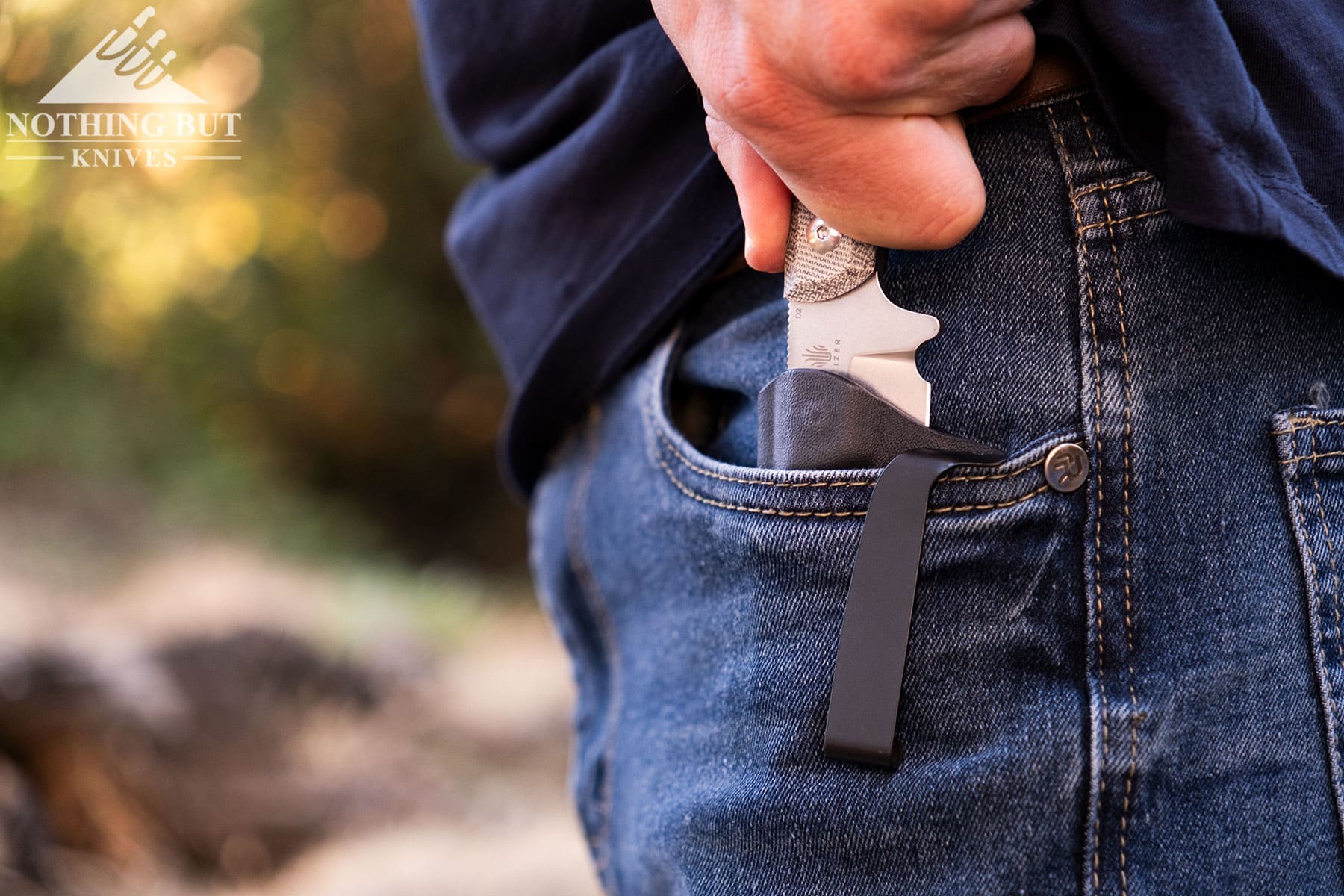 A close-up of the Kizer Deckhand being carried as an EDC fixed blade in a person's left pocket. 