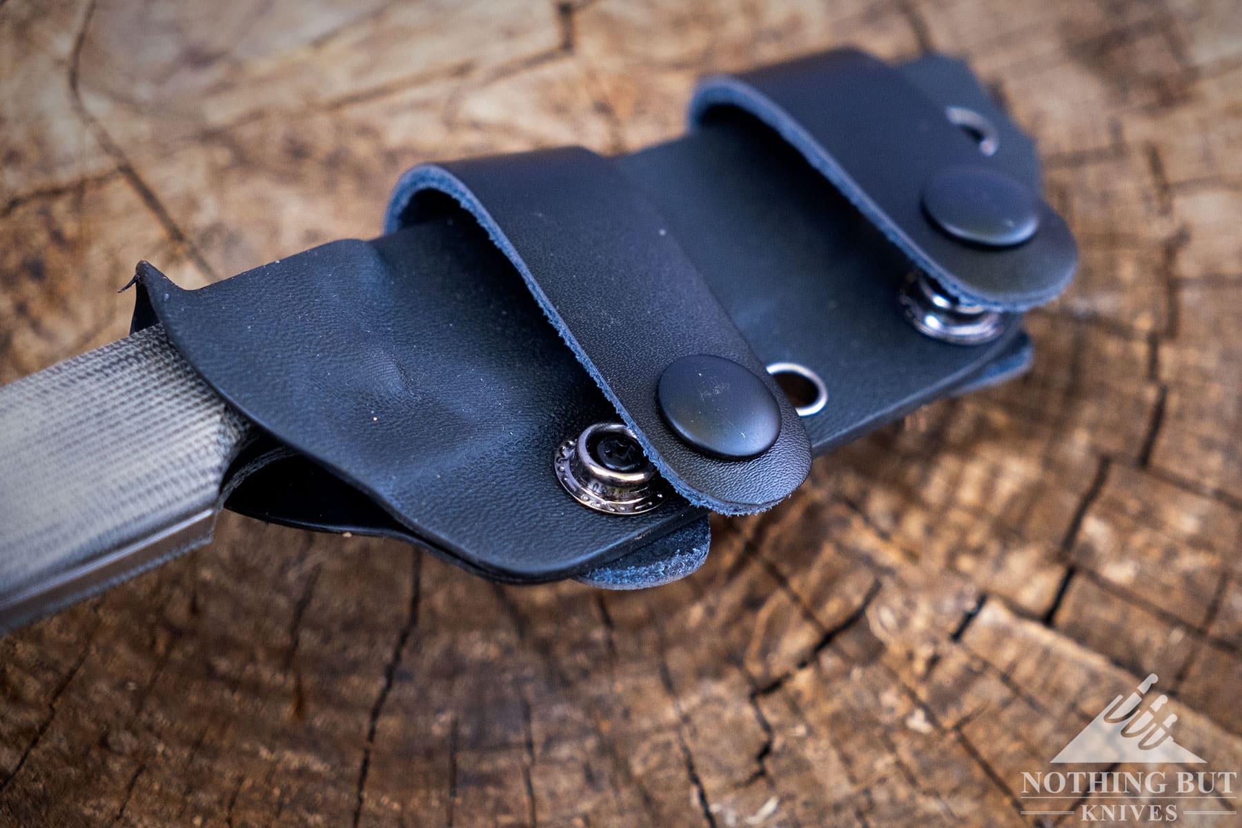 An overhead shot that shows a Kizer sheath with leather horizontal carry strap being lifted off a tree stump. 