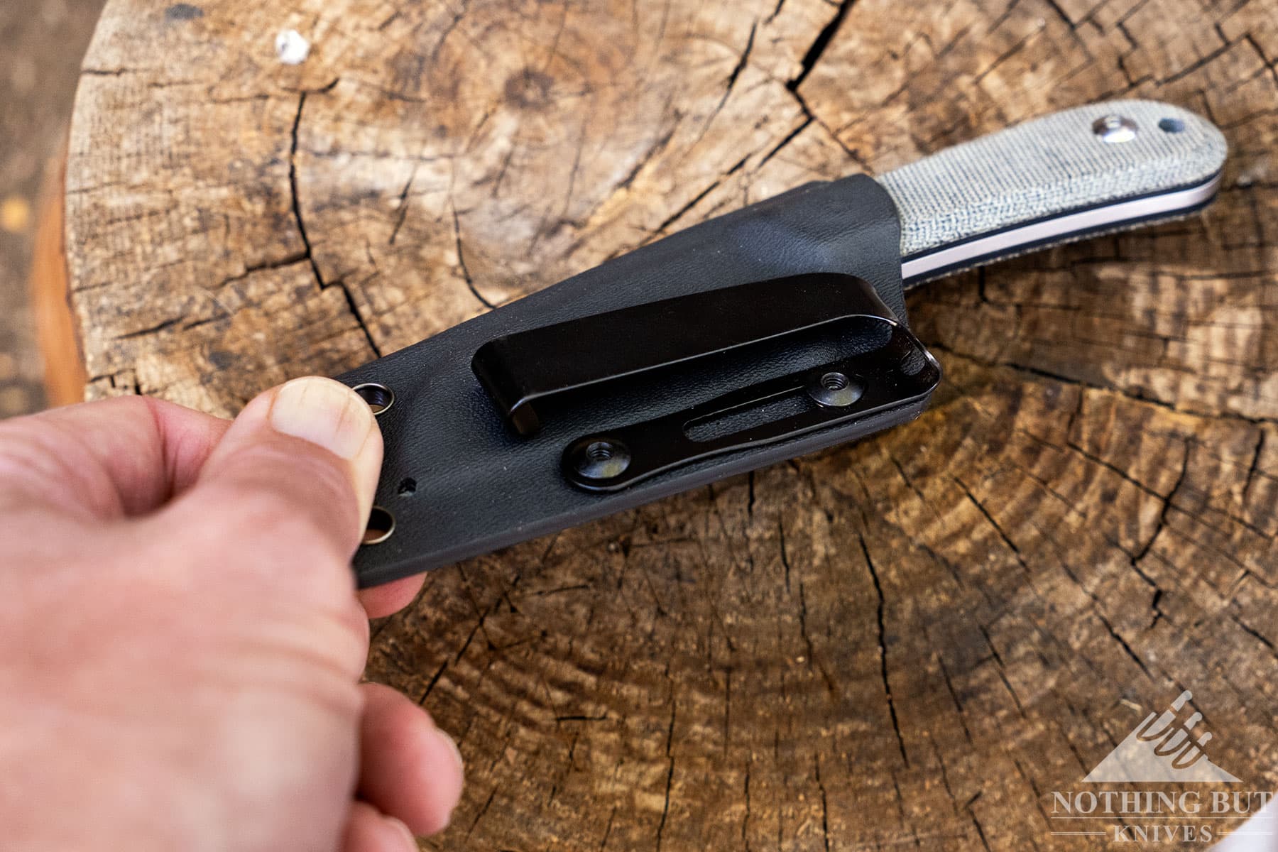 An overhead view of a Kizer sheath being lifted of a tree stump to show its G Clip for EDC pocket carry.