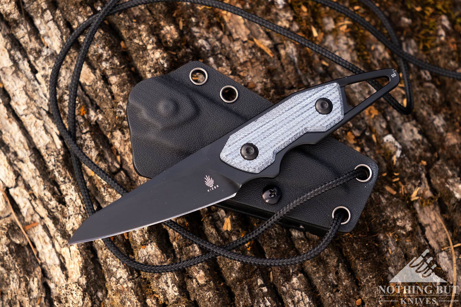 An Overhead view of the Kizer Groom compact fixed blade with its kydex sheath and lanyard on a tree stump. 