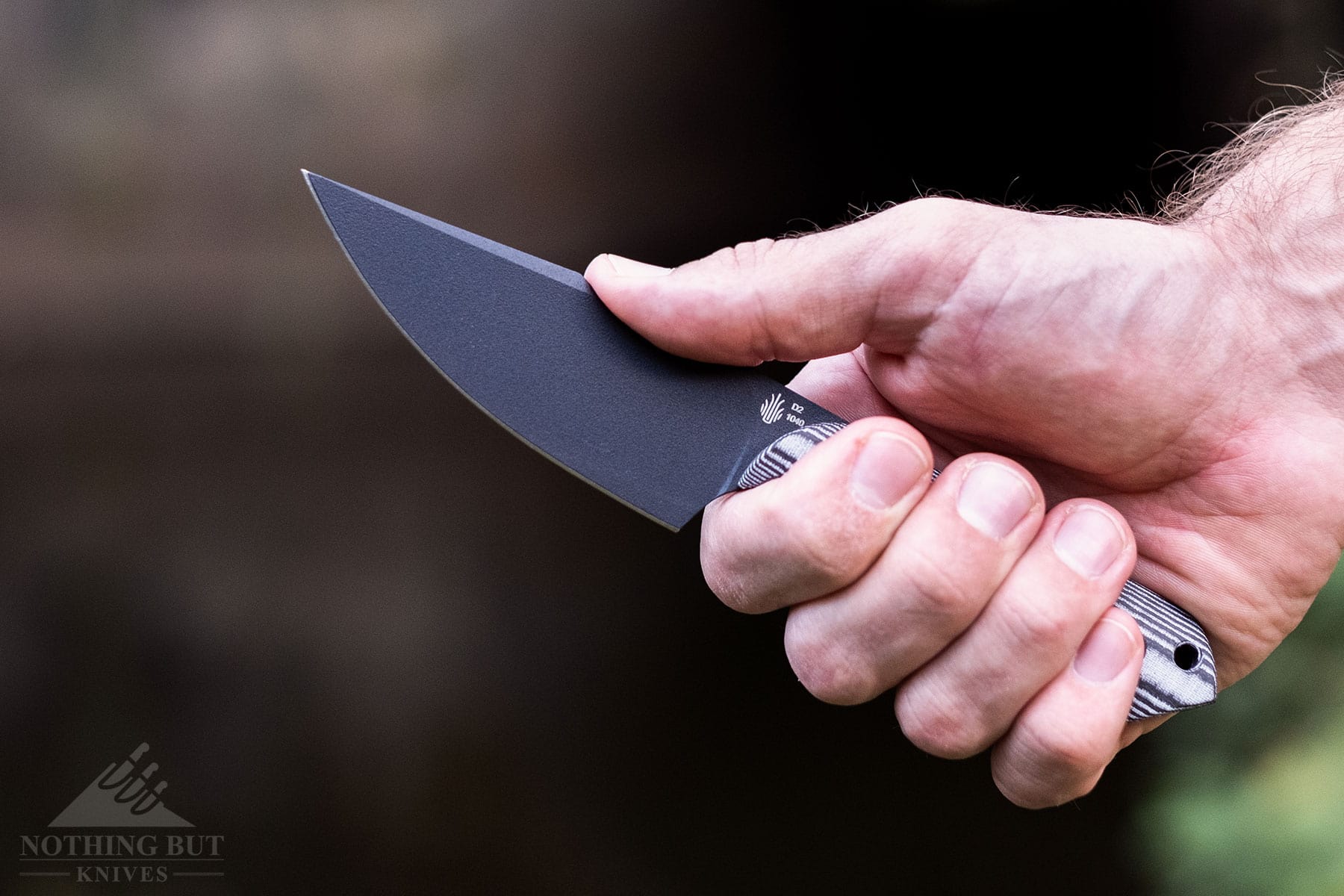 A close-up of a person's right hand gripping the handle of the Kizer Harpoon fixed blade knife. 