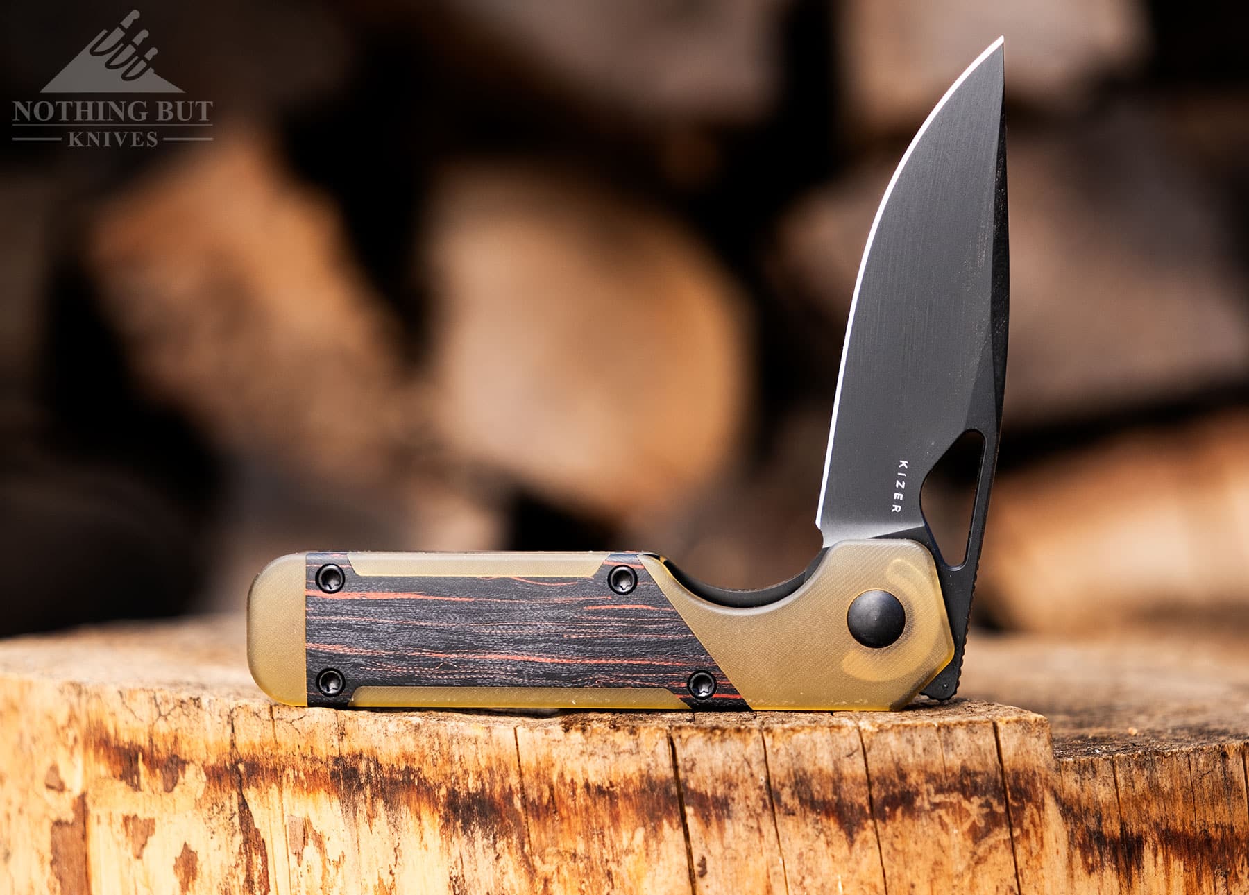 The Kizer Mini Militaw folding knife in with the blade in the half open position on a tree stump. 