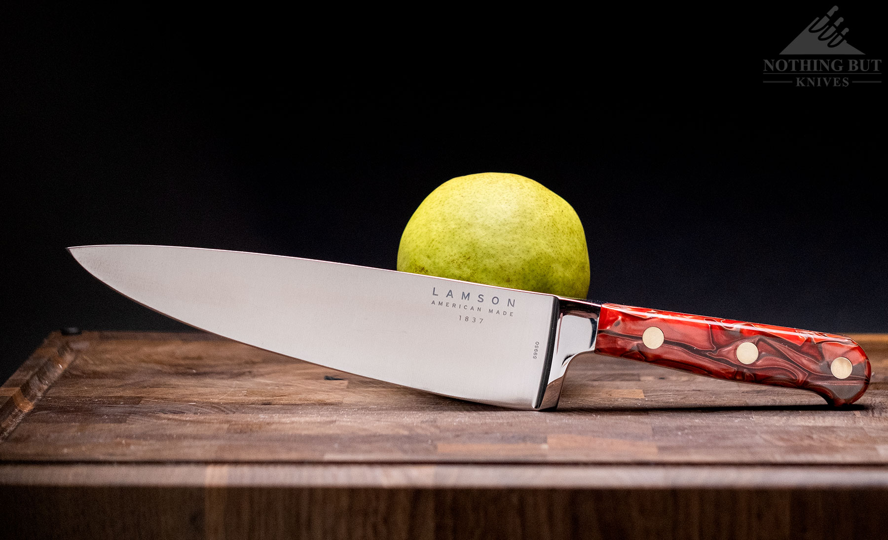 The Lamson Premier chef knife leaning against an apple on an end grain cutting board in front of a dark background.