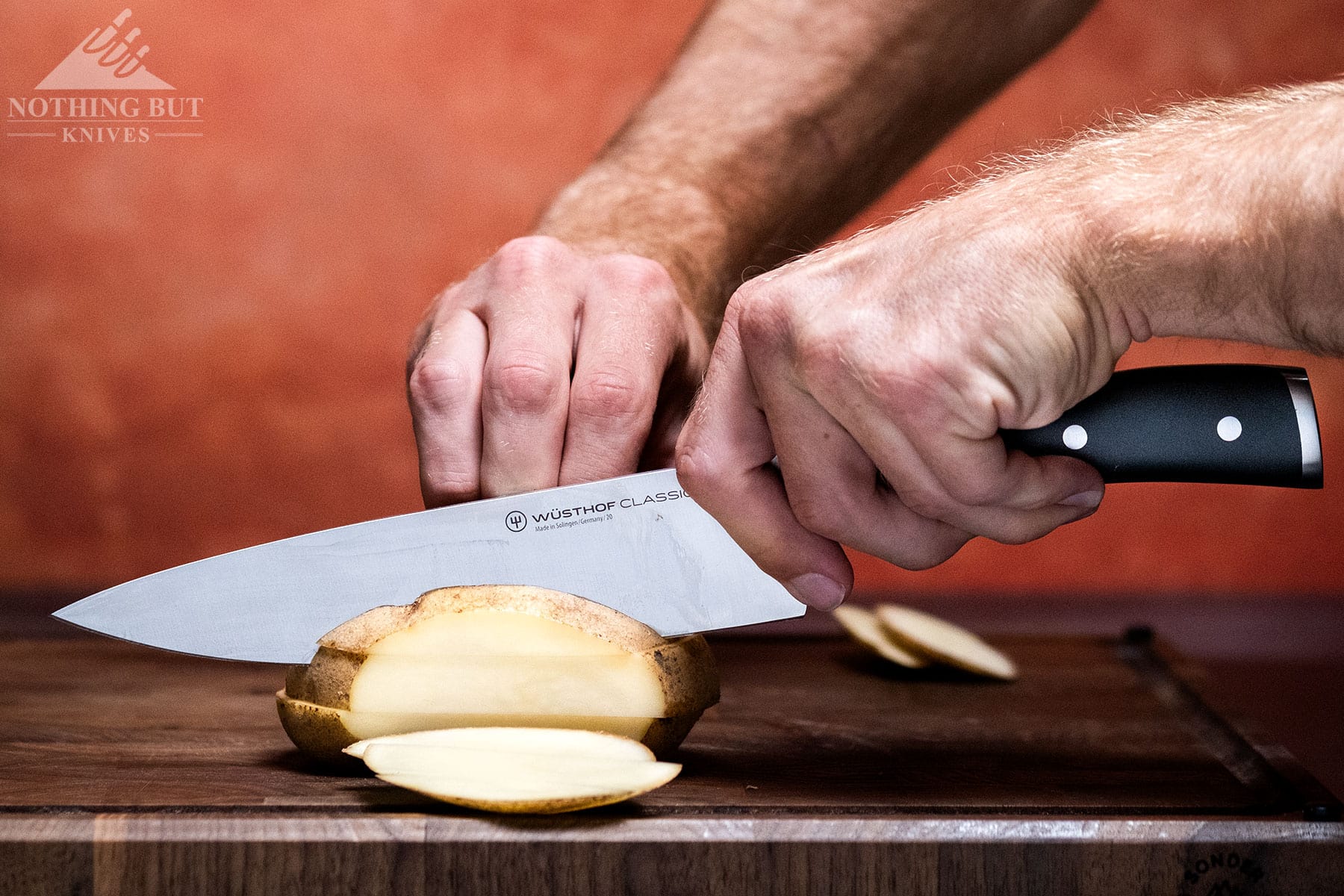 A potato being sliced with the Wusthof Classic Ikon chef knife in front of a maroon background. 