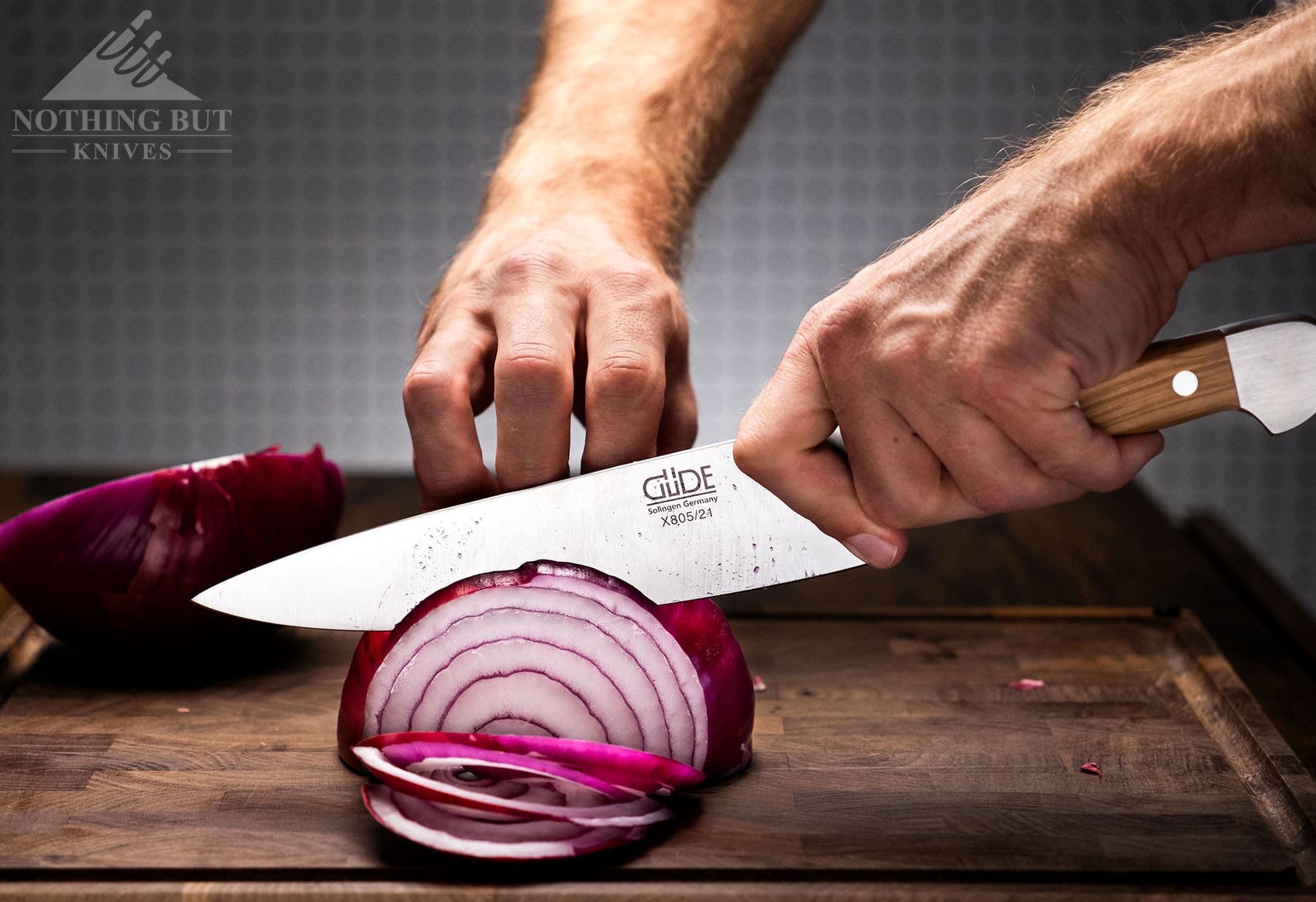 The Gude 8 inch chef knife being used to slice an onion on top of an end grain cutting board.