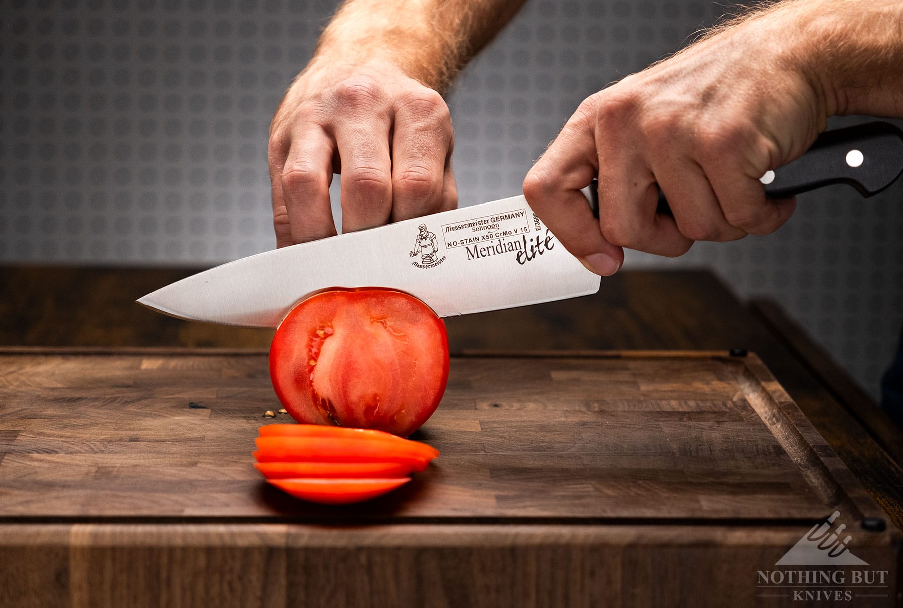 The Messermeister Elite German made chef knife being used to slice a tomato on a wood cutting board. 