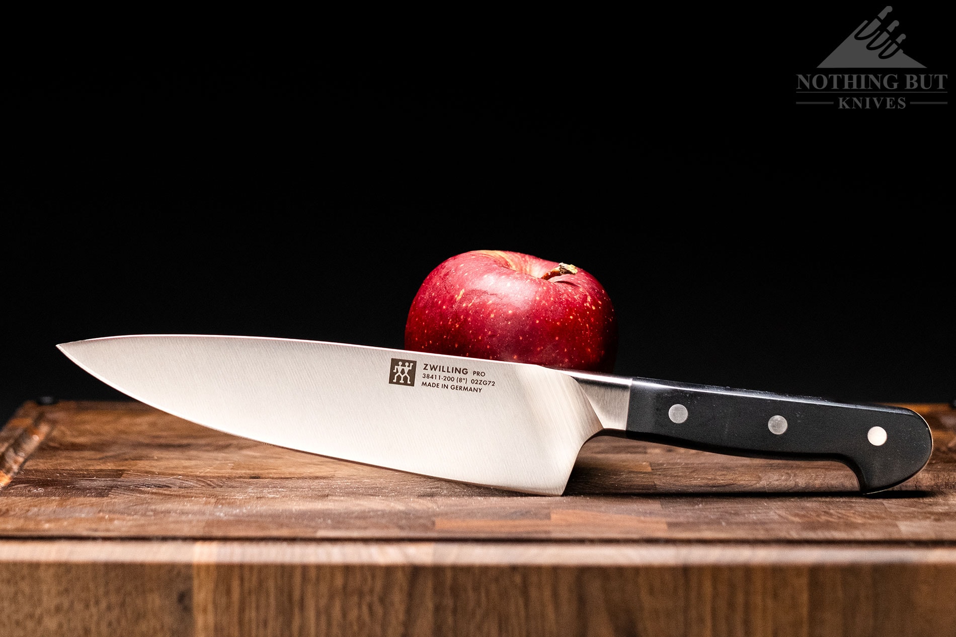 The Zwilling Pro German chef knife leaning against an apple on an end grain cutting board. 