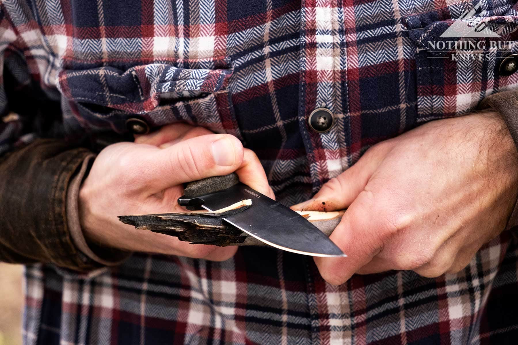 A close-up of the LIonSteel M5 being used in the chest lever grip to carve a small branch. 