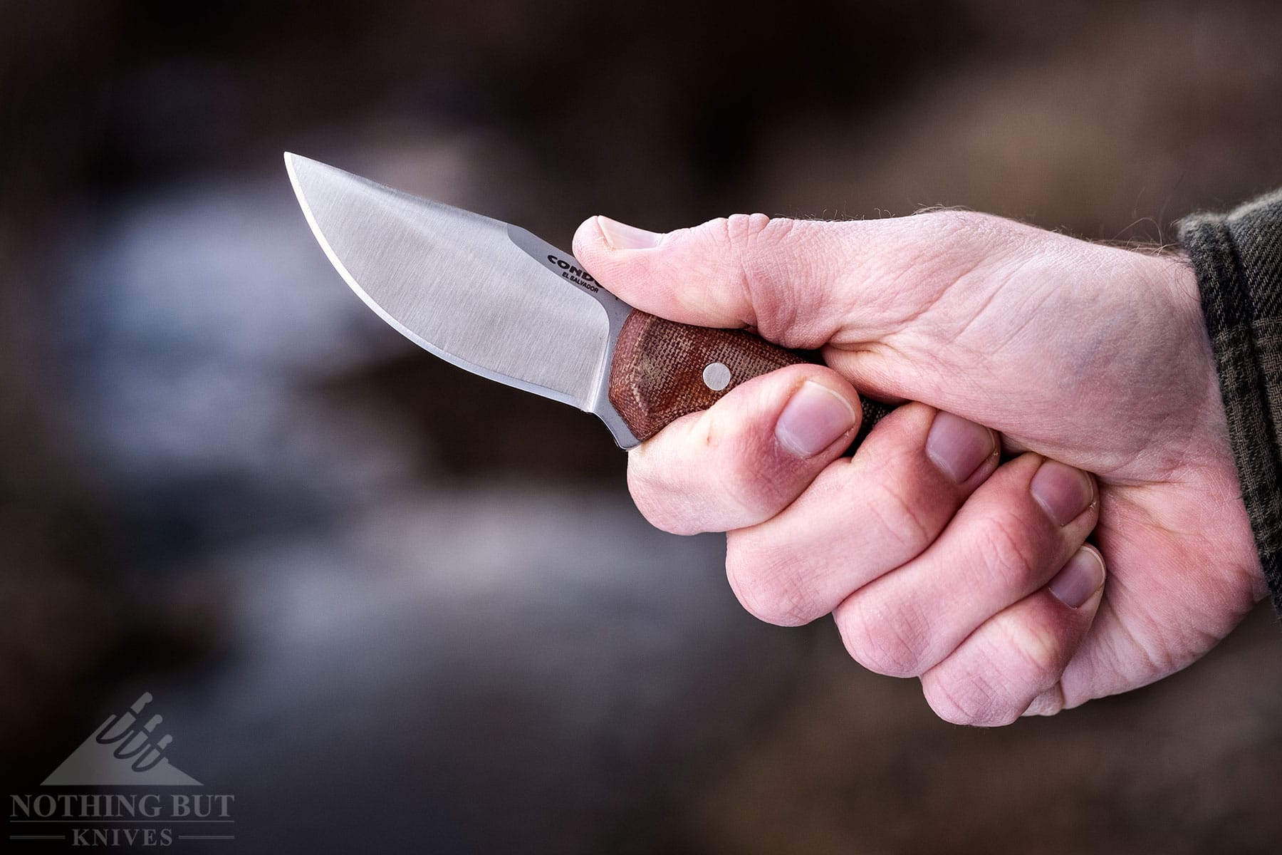 The Condor Mountaineer Trail Wingman being held in a person's right hand in front of a creek to show handle scale and ergonomics.